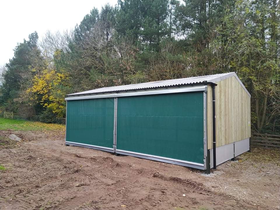 A green shed is sitting in the middle of a dirt field.