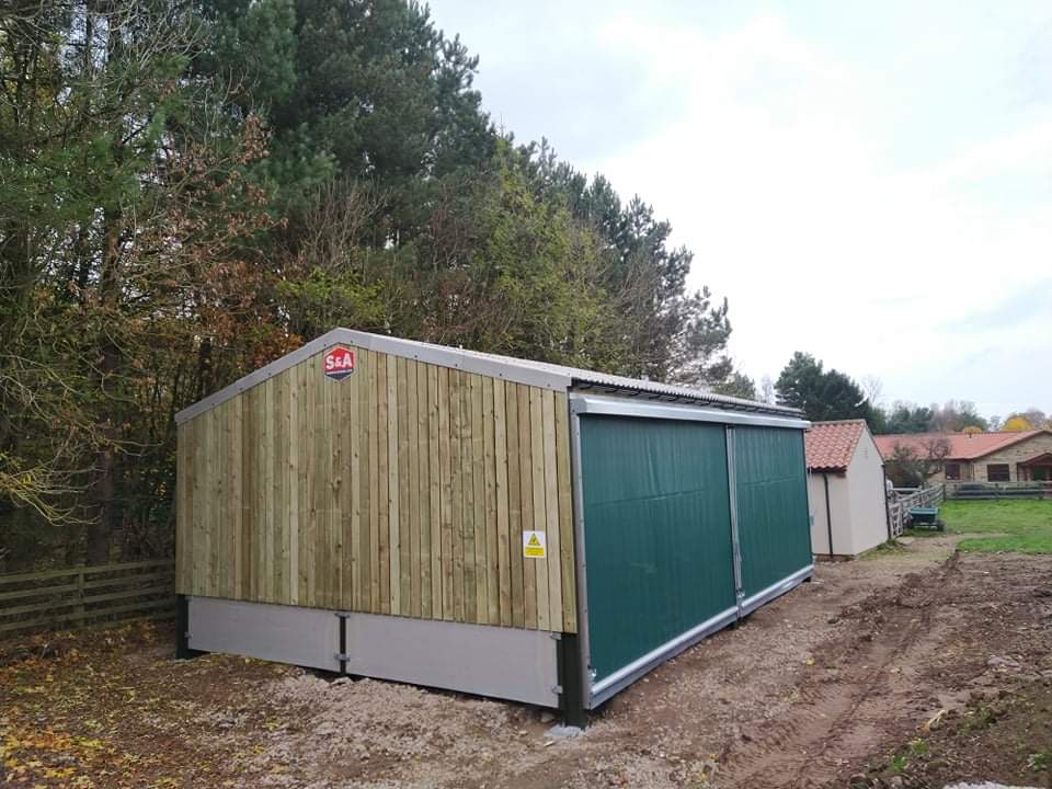 A wooden building with a green door is sitting in the middle of a dirt road.