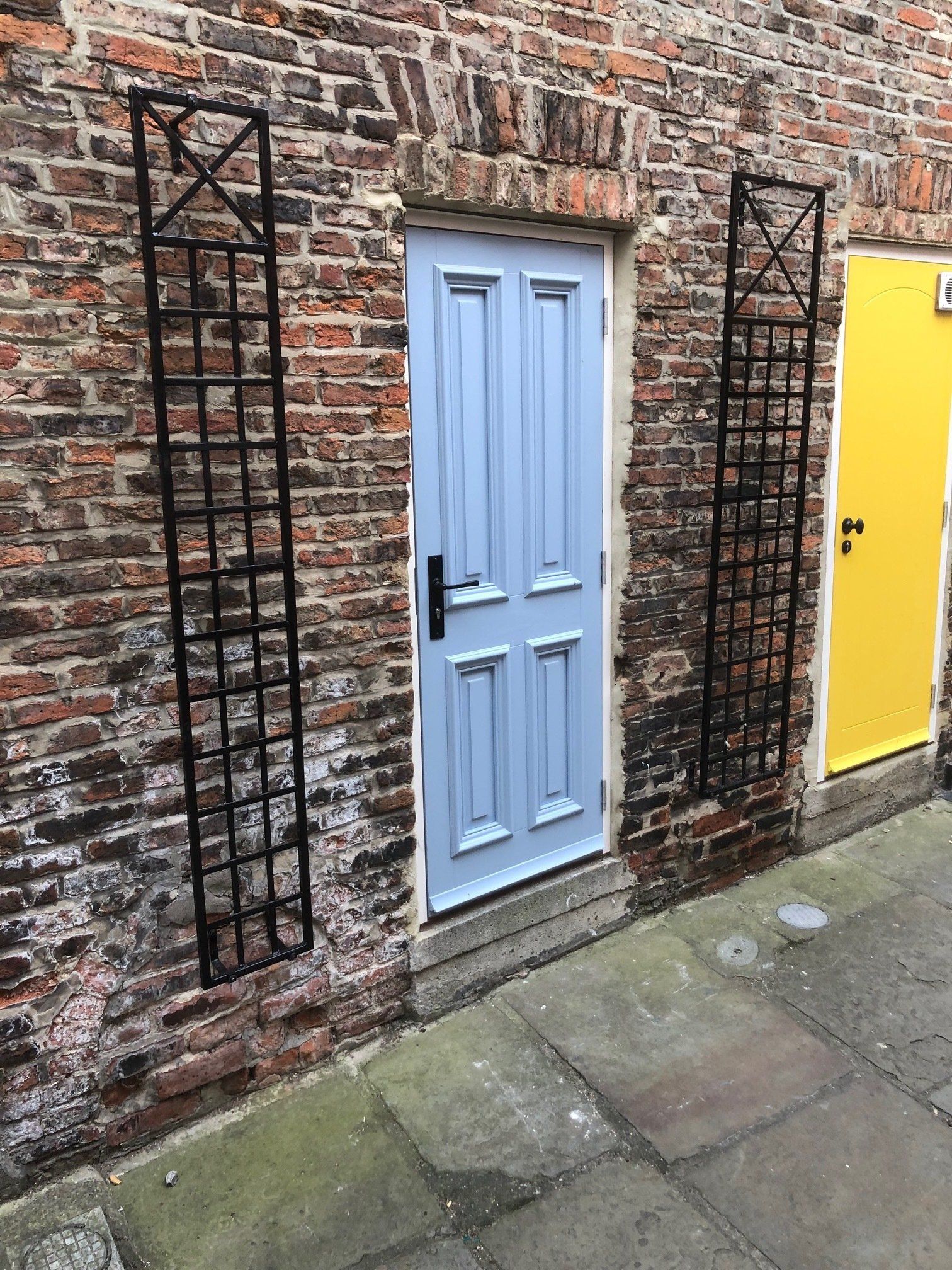 A blue door is next to a yellow door on a brick wall.