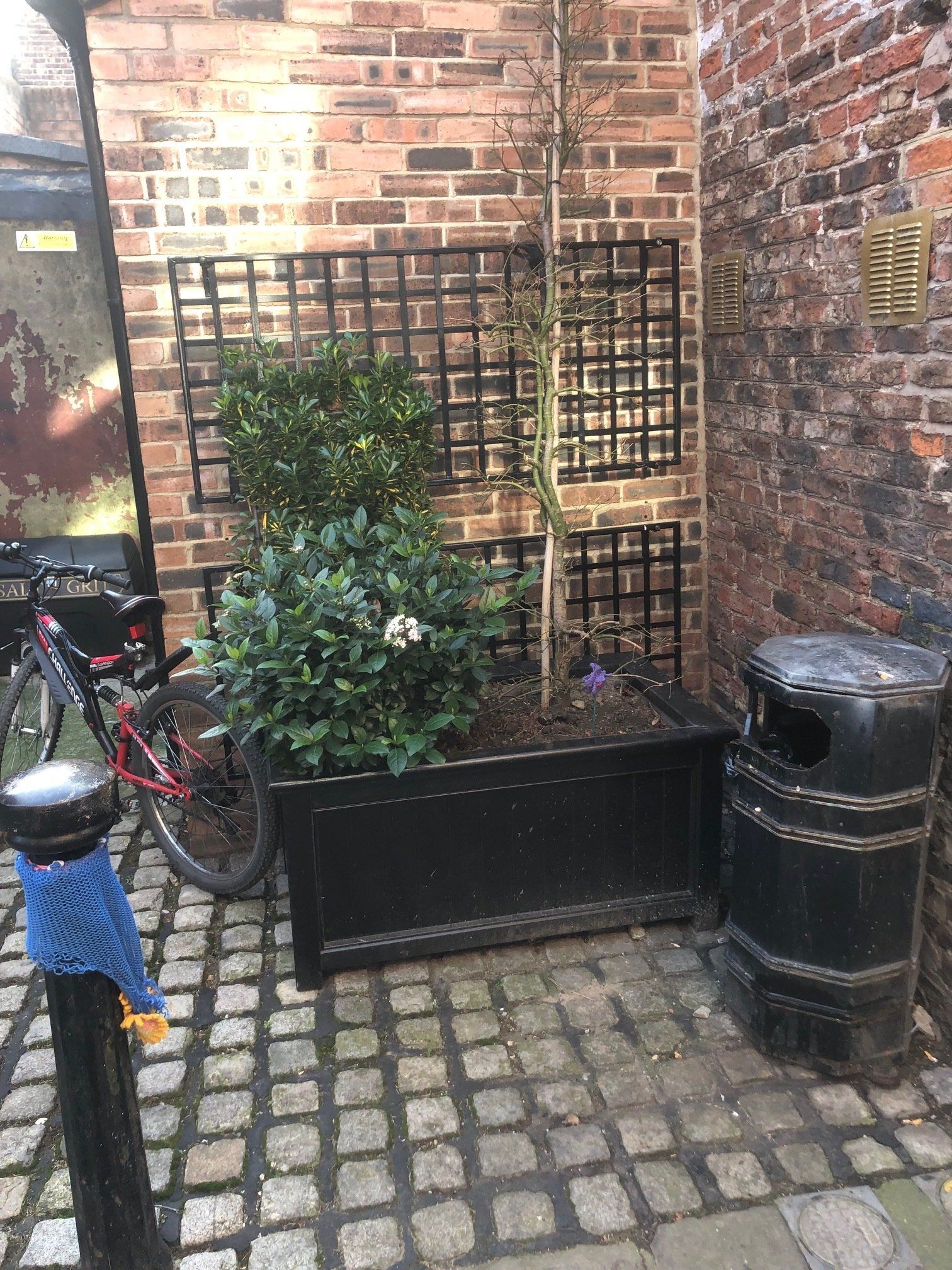 A bicycle is parked in front of a brick wall next to a trash can.