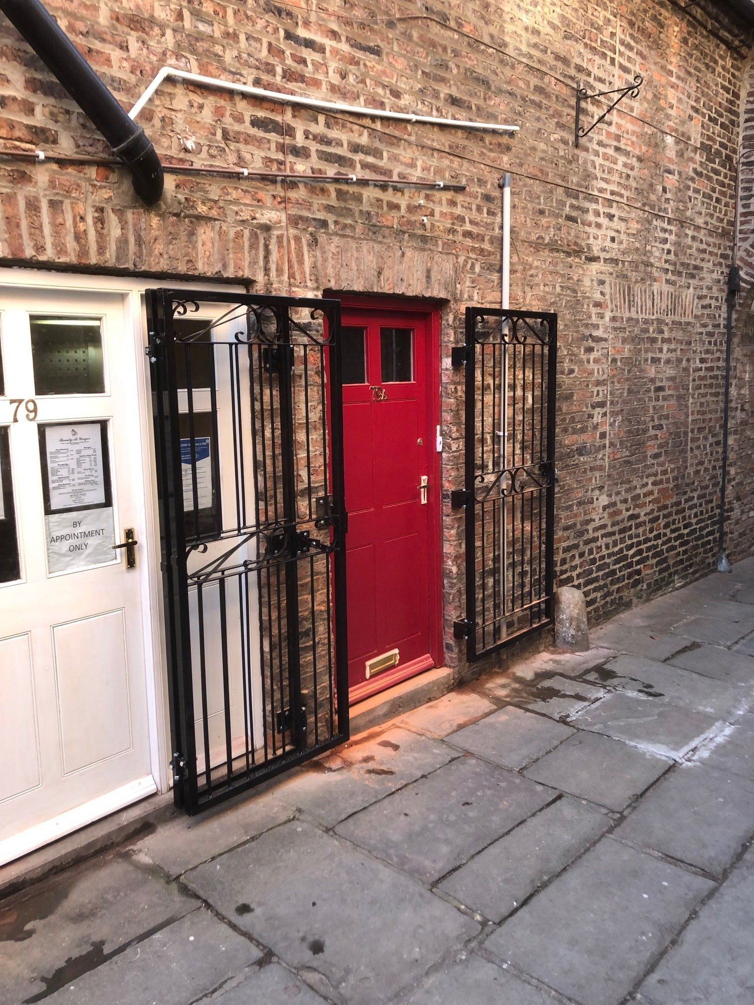 A red door is behind a black gate in front of a brick building.