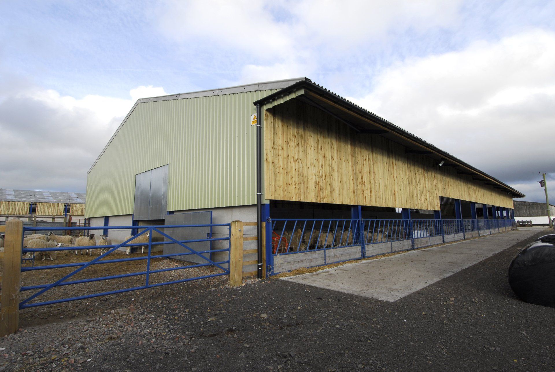 A large building with a blue fence around it is surrounded by gravel.