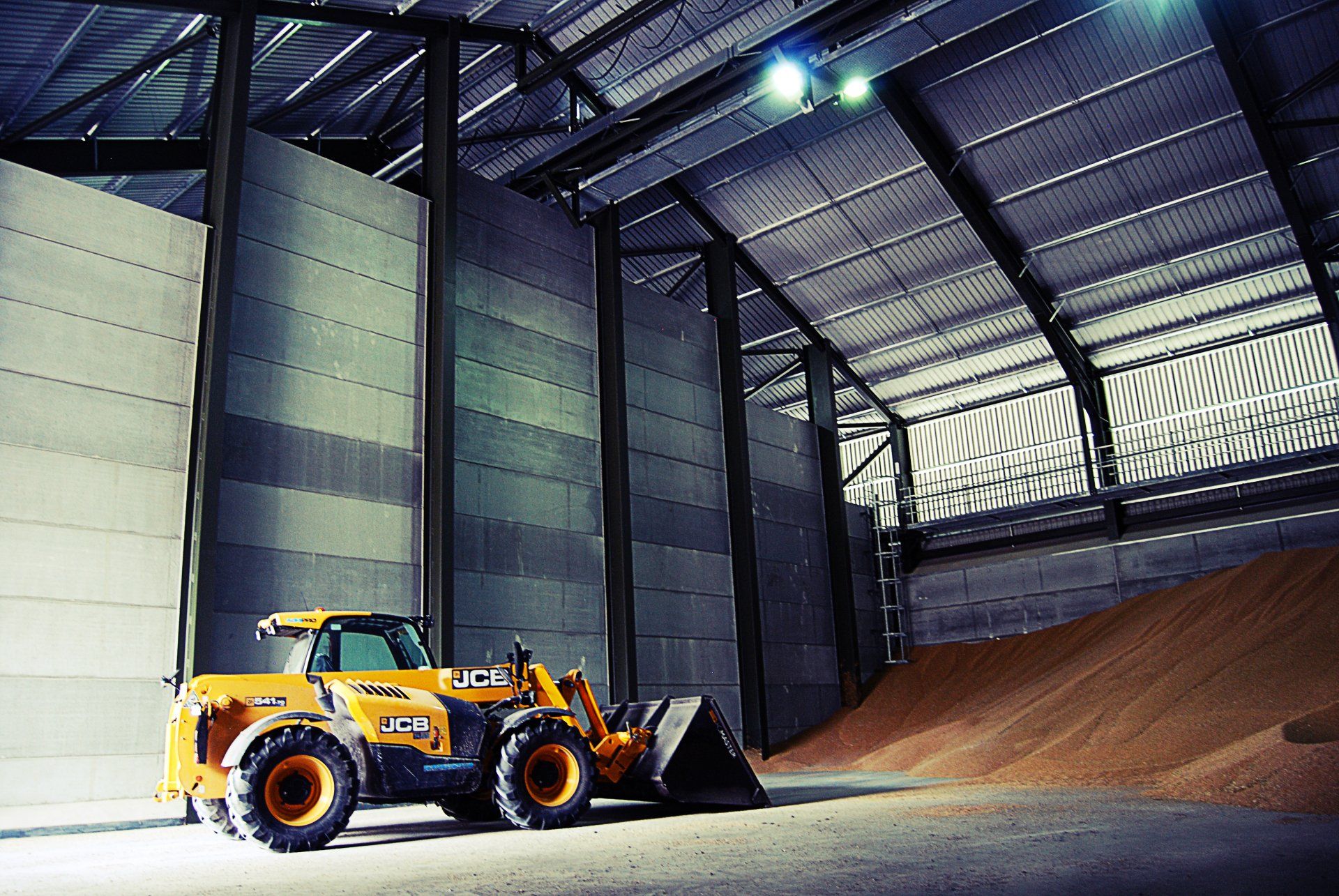 A yellow jcb tractor is parked in a large warehouse