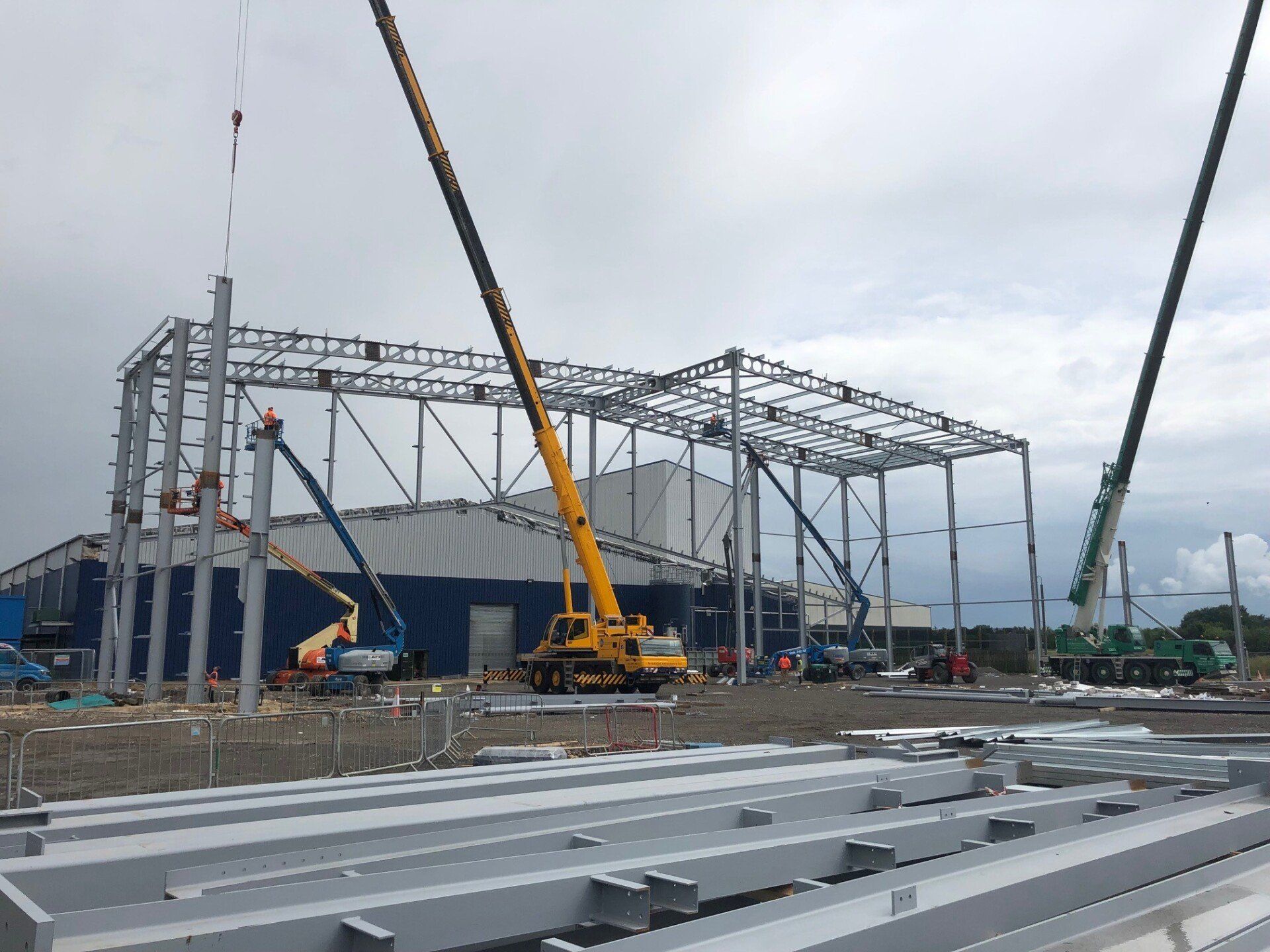 A yellow crane is lifting a metal structure in front of a building under construction.