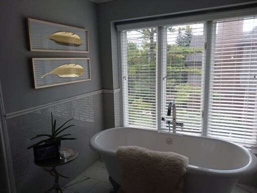 Bright bathroom with a freestanding tub, large window blinds, and framed fish artwork on gray walls