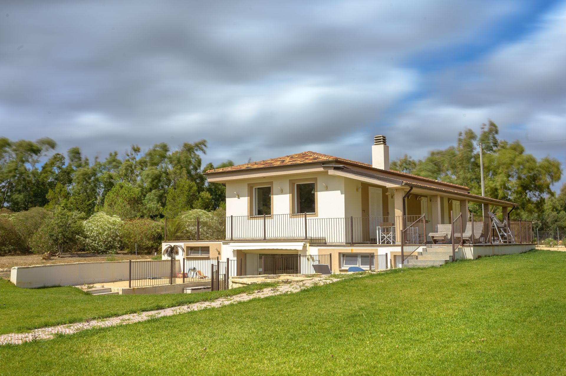 Casa bianca con tetto di tegole, balcone e cortile erboso sotto un cielo nuvoloso.