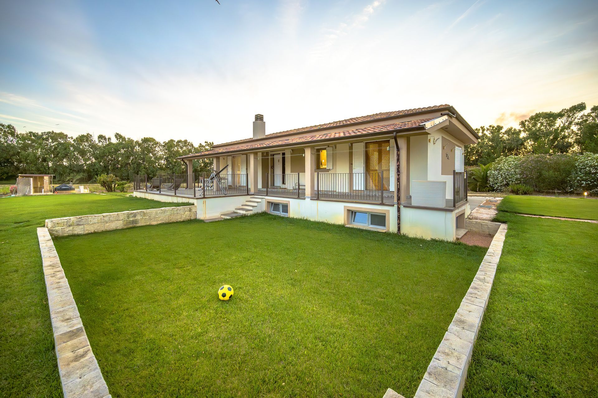 Una casa a un solo piano con tetto di tegole e ampio portico in un cortile erboso al tramonto.