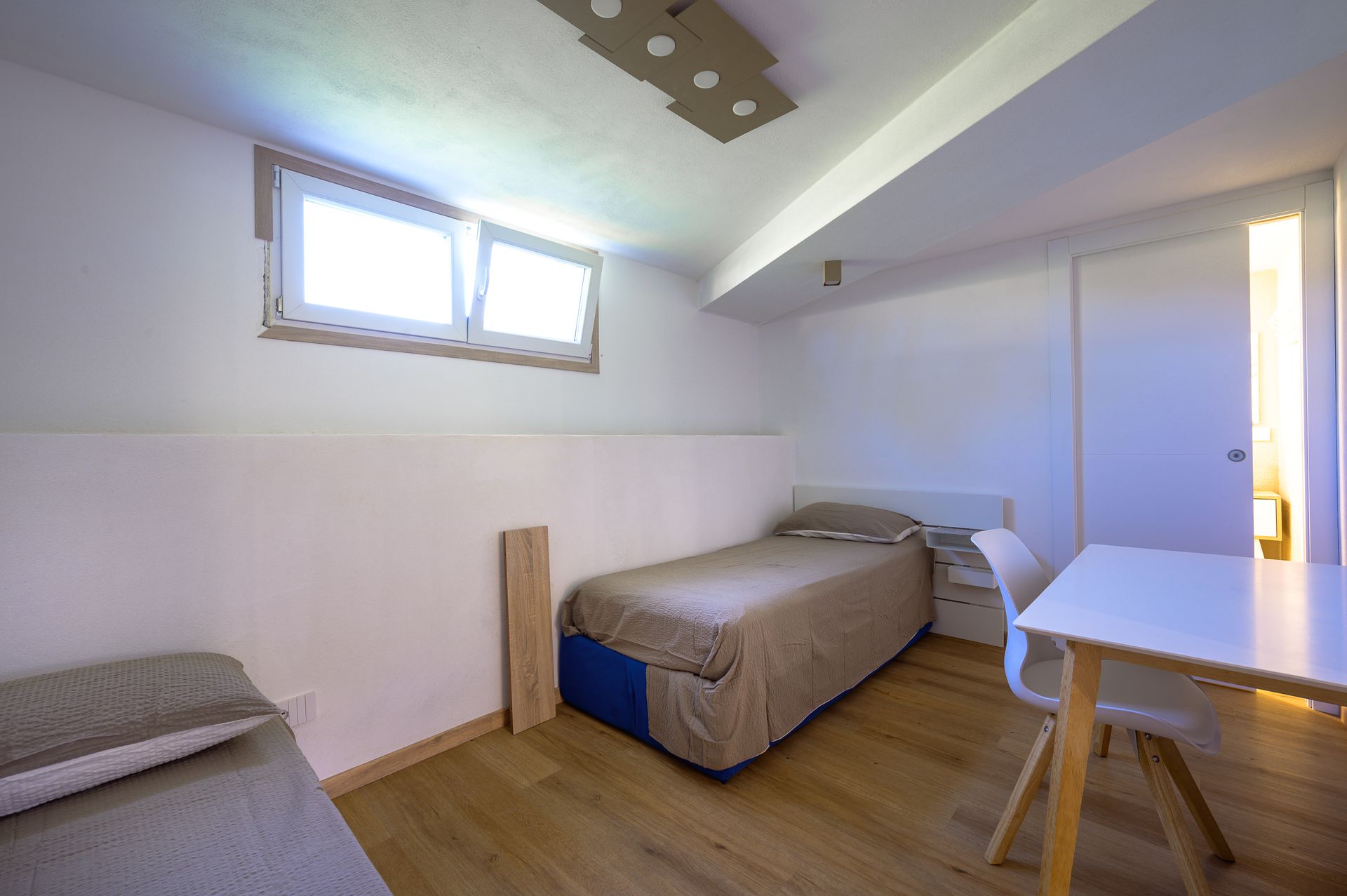 Camera da letto con due letti, una scrivania e una finestra. Pareti bianche e pavimento in legno.