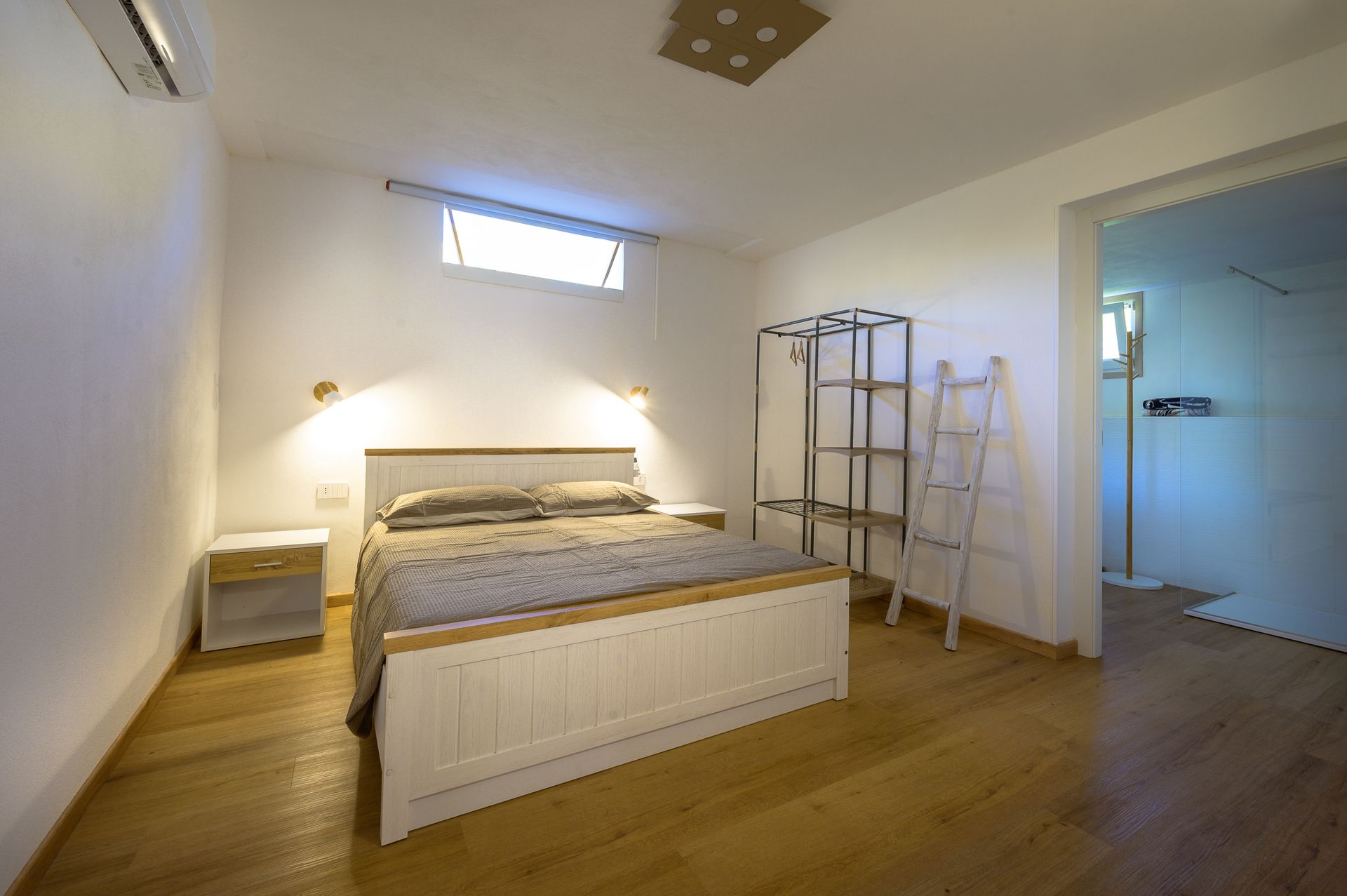 Camera da letto con letto bianco, pavimenti in legno chiaro e una porta che conduce a un'altra stanza.