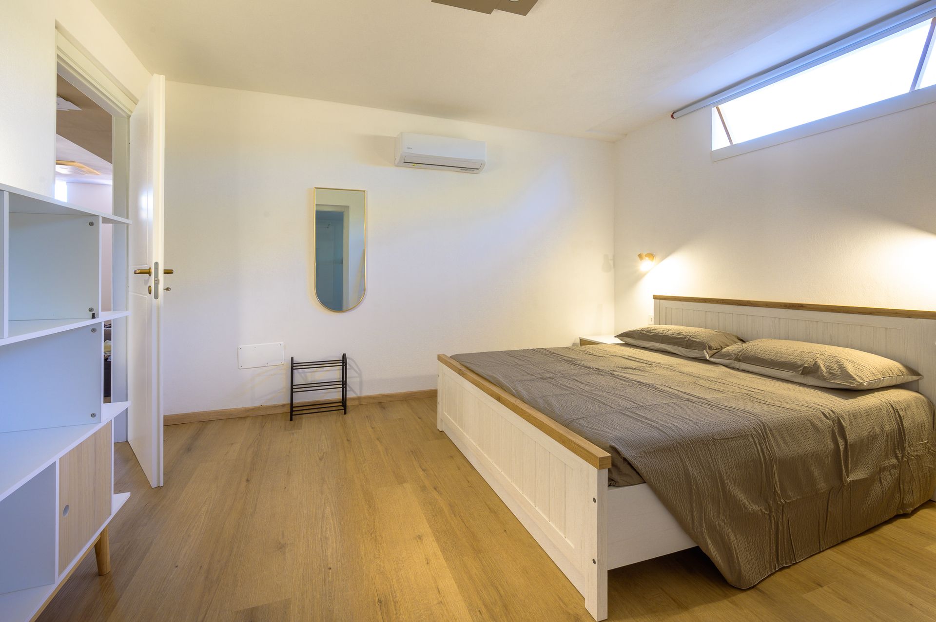 Camera da letto con pareti bianche, un letto, uno specchio e un armadio. Pavimento in legno chiaro.