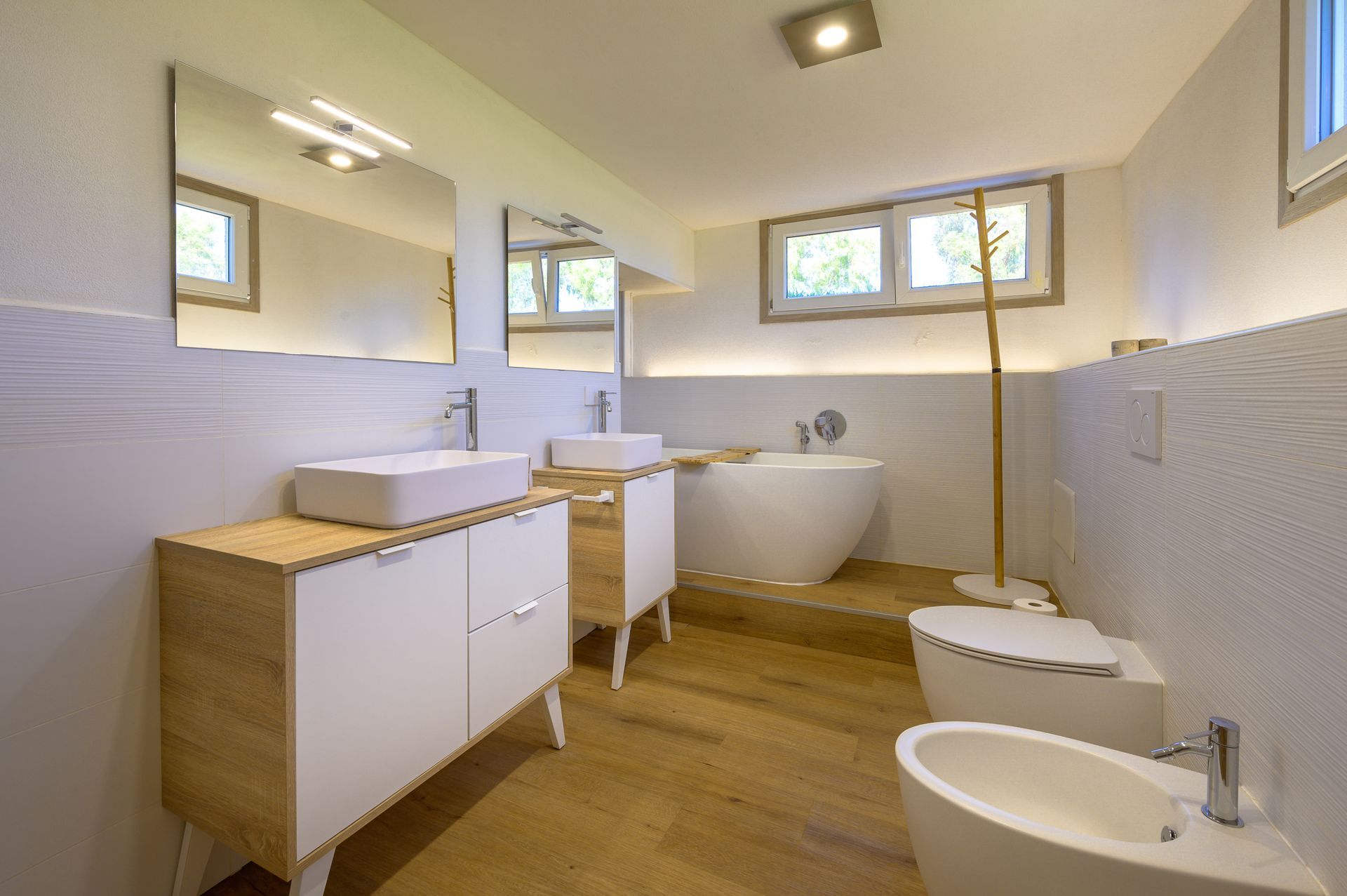 Bagno moderno con pavimento in legno, sanitari bianchi e due lavandini.