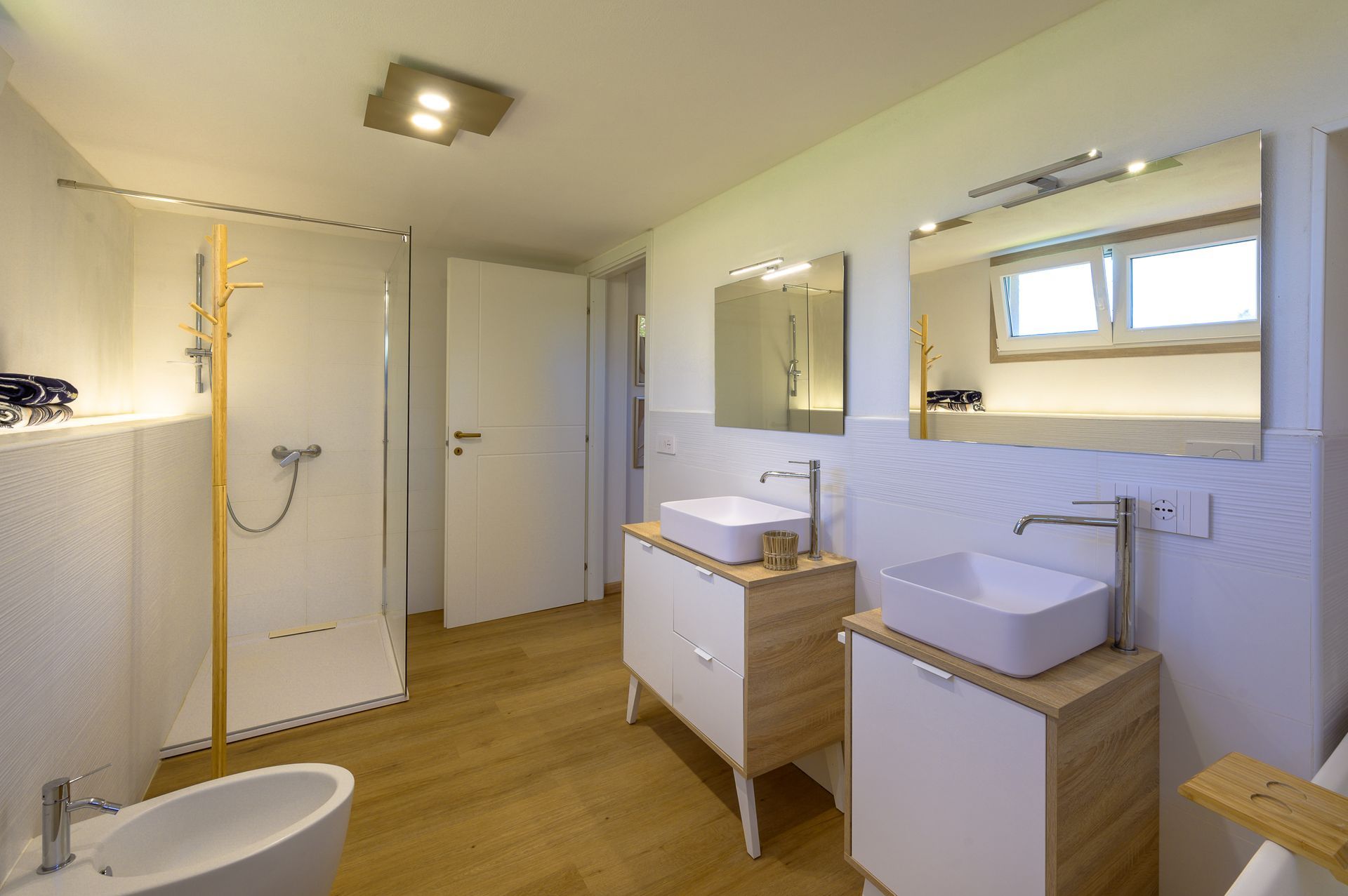 Bagno moderno con pareti bianche, pavimento in legno e due lavandini con specchi.