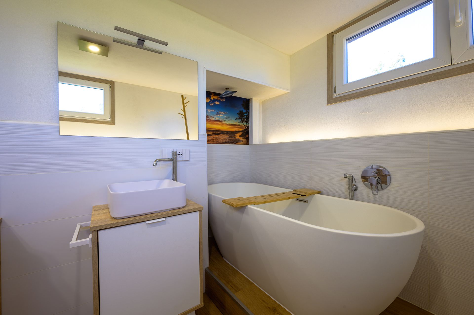 Bagno moderno con pareti bianche, vasca indipendente e piccolo mobile lavabo.