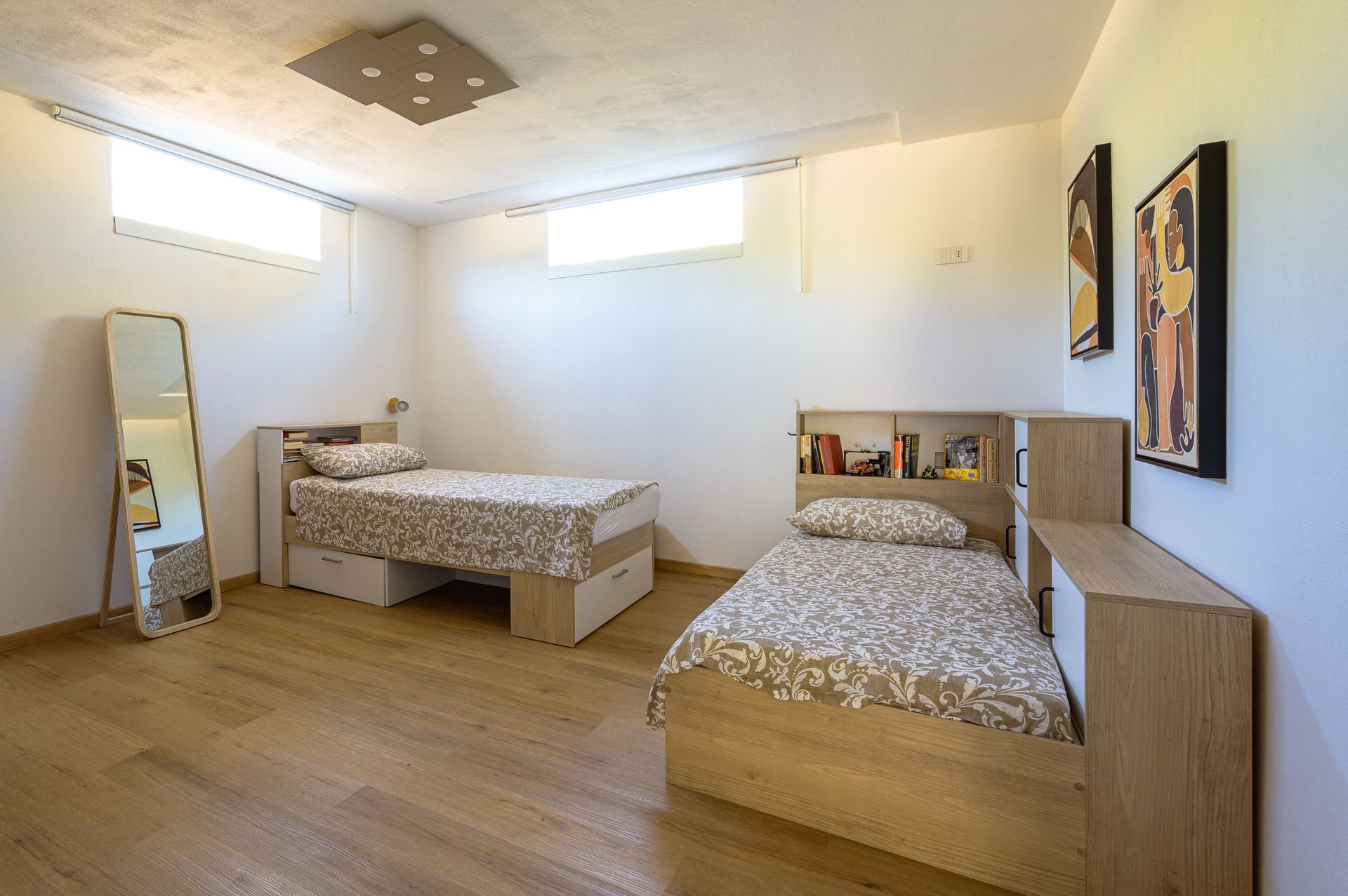 Camera da letto con due letti, uno specchio a figura intera e quadri incorniciati alla parete, con pavimento in legno.