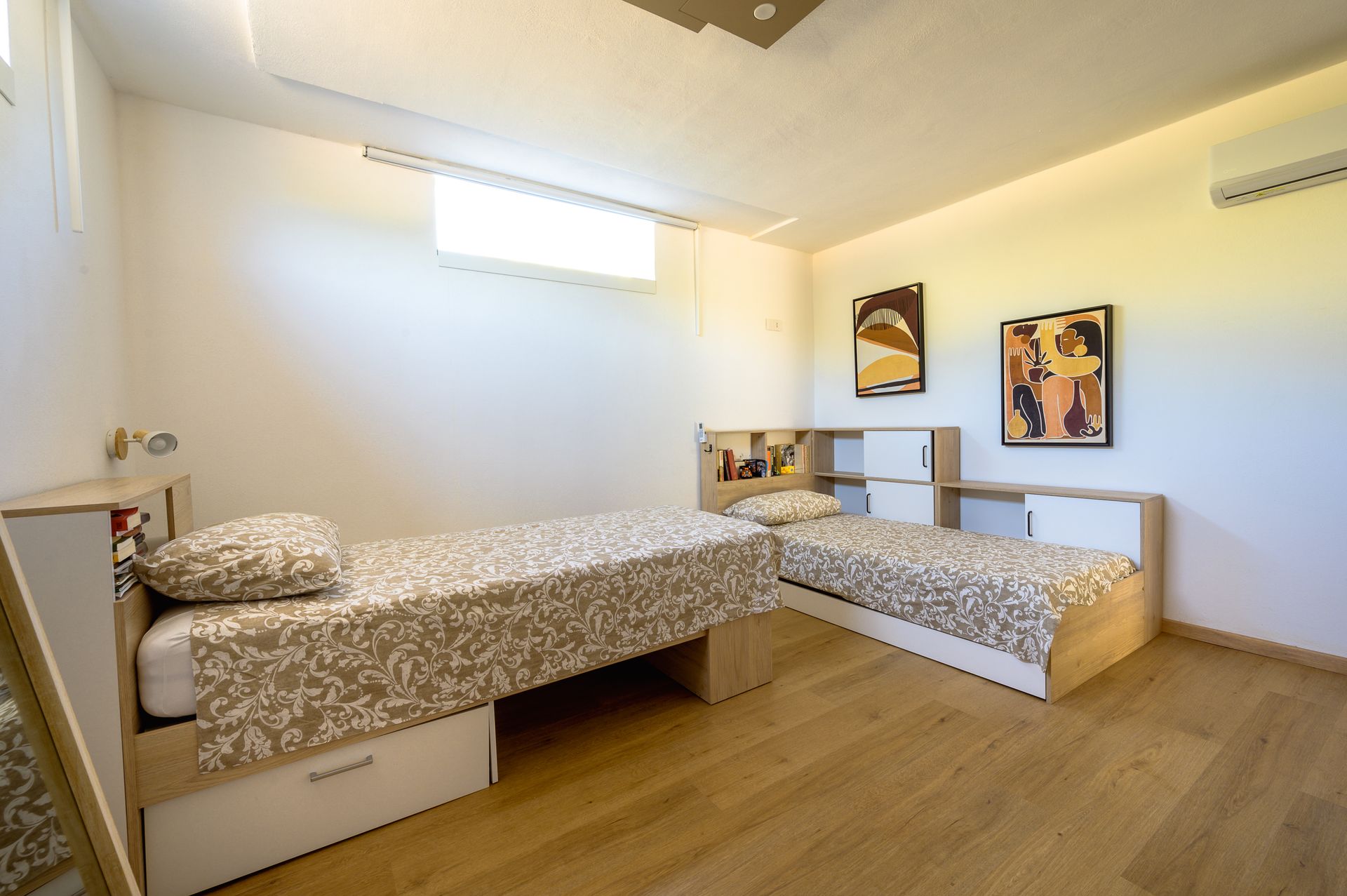 Due letti singoli in una moderna camera da letto con pavimenti in legno chiaro e due poster incorniciati alla parete.