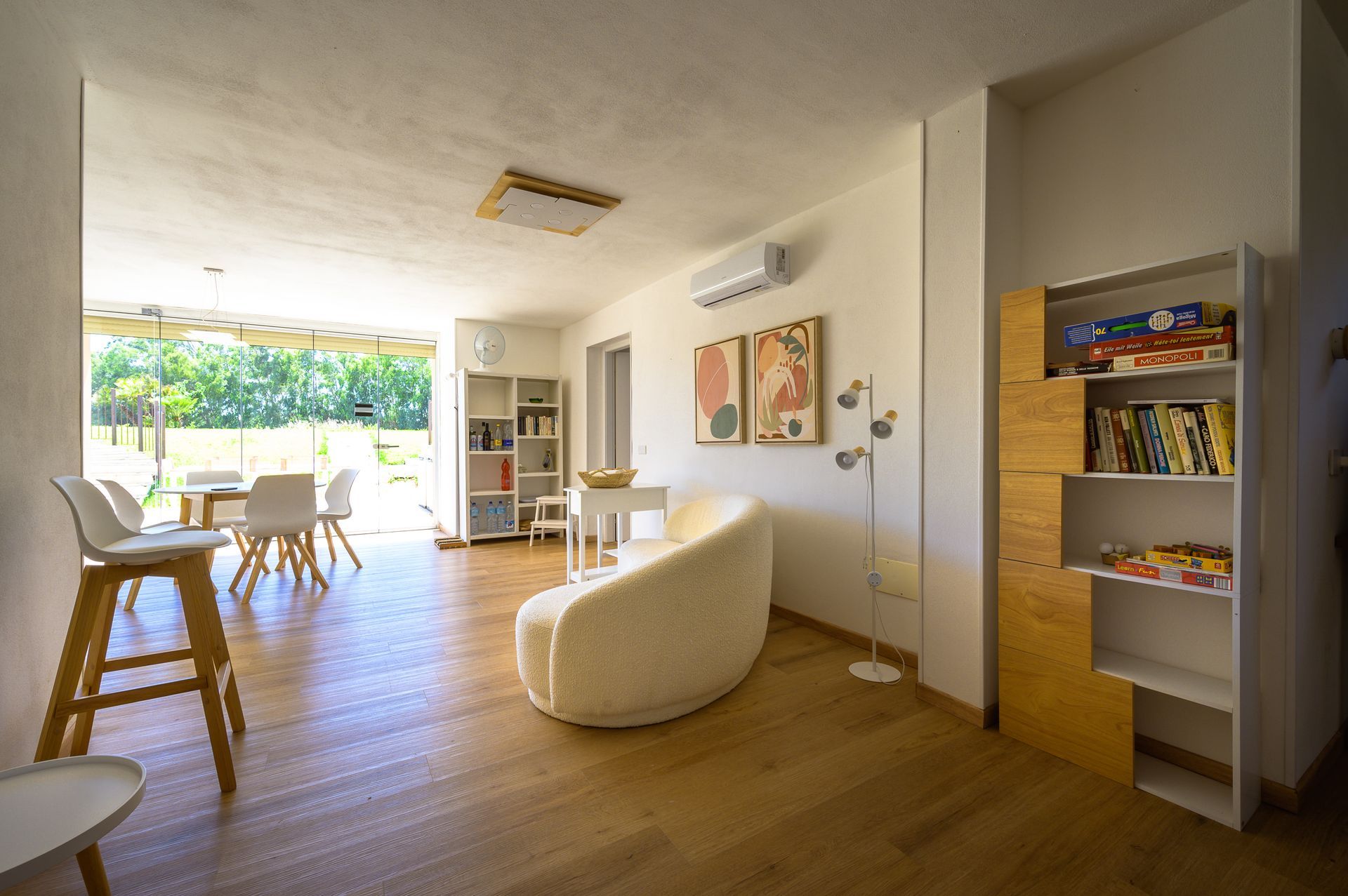 Luminoso soggiorno con pareti bianche, pavimento in legno e vista sul giardino. Dispone di divano bianco, librerie e tavolo da pranzo.