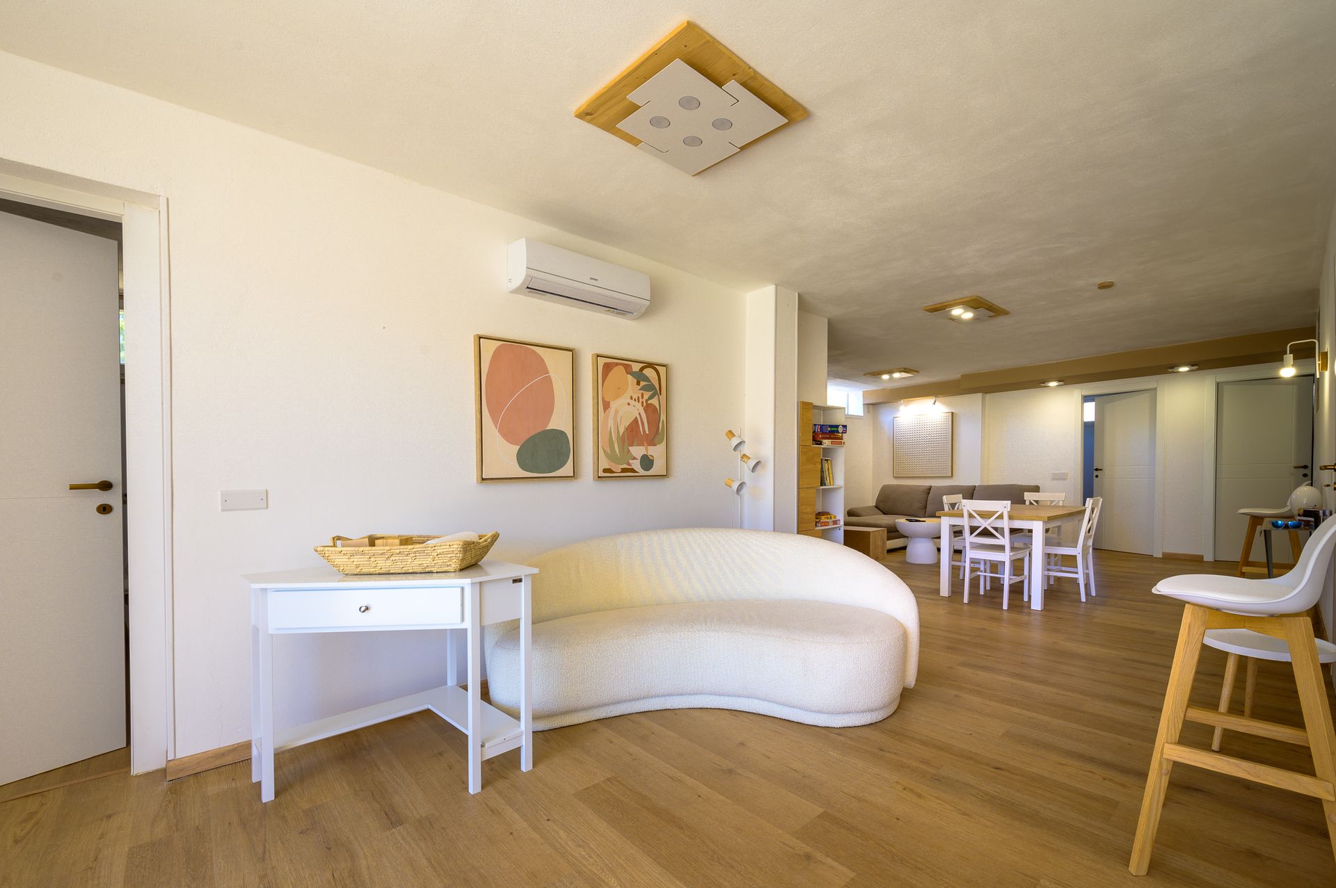 Luminosa zona giorno con divano bianco curvo, opere d'arte e un tavolo da pranzo visibile sullo sfondo.