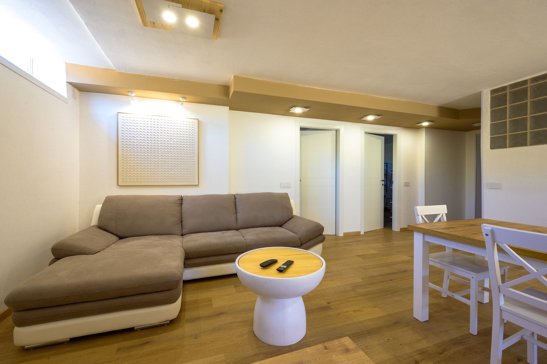 Soggiorno con divano componibile marrone, tavolo in legno e pareti bianche.