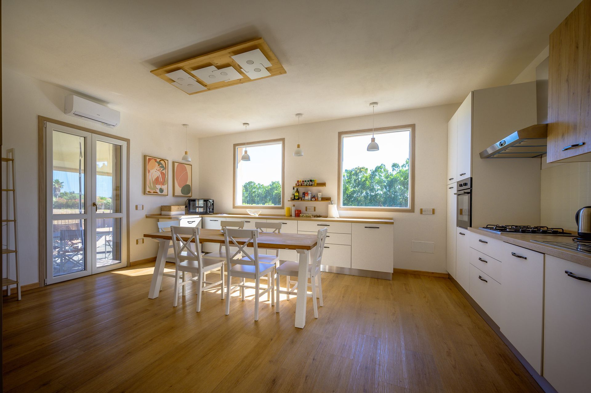 Cucina luminosa con mobili bianchi, pavimento in legno e tavolo con sedie.