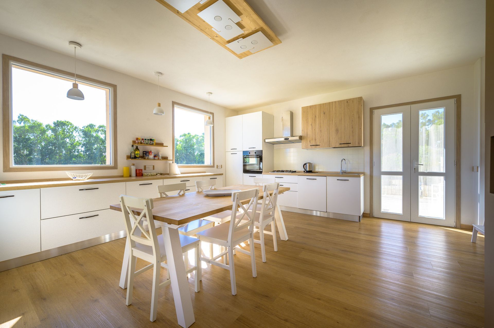 Cucina luminosa con pavimenti in legno, mobili bianchi e un tavolo in legno con sedie bianche.