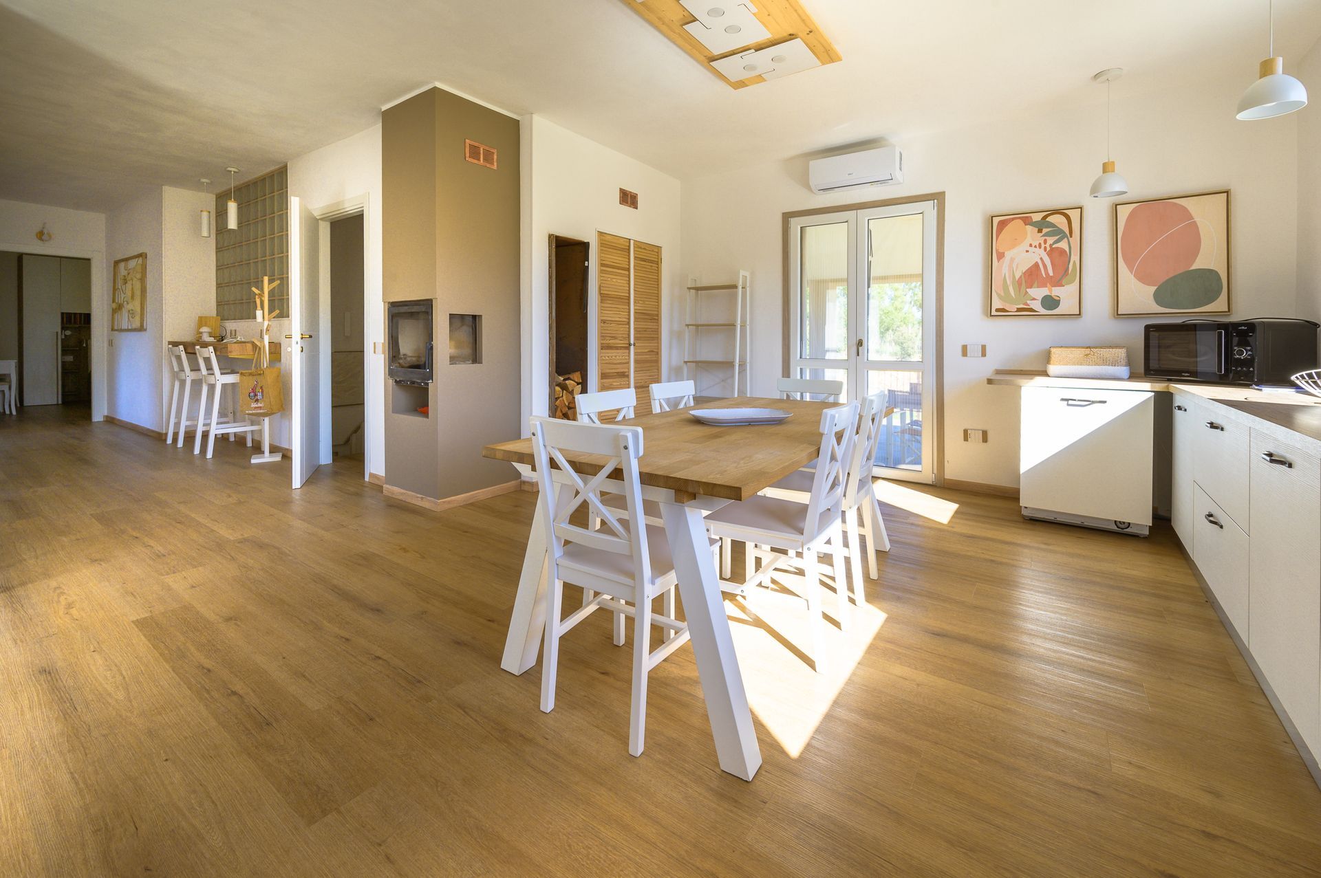 Luminosa cucina/sala da pranzo open space con pavimenti in legno, mobili bianchi e luce solare che filtra all'interno.