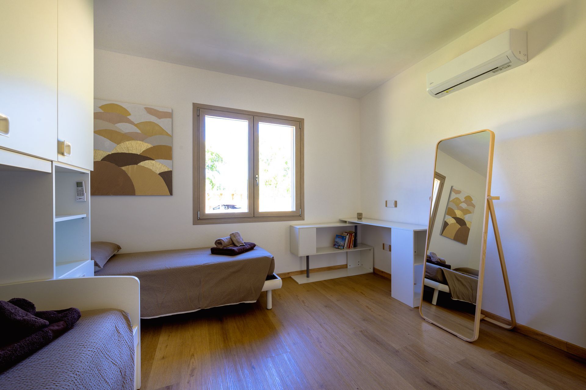 Camera da letto con due letti, scrivania, specchio, opere d'arte, finestra e pavimento in legno.