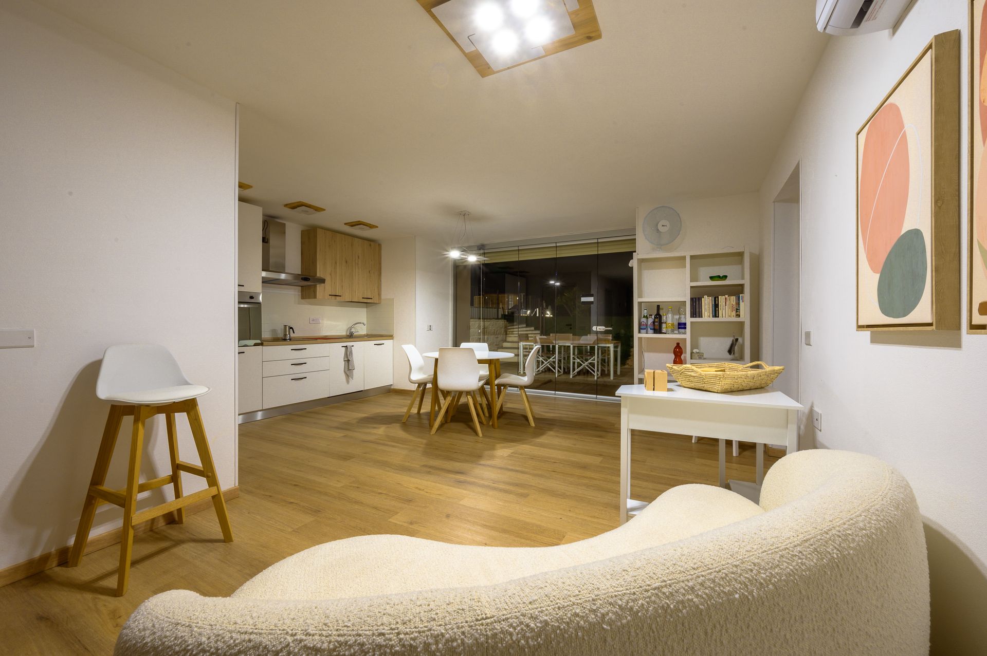 Accogliente soggiorno con cucina. Divano bianco, pavimenti in legno, toni neutri e opere d'arte alle pareti.