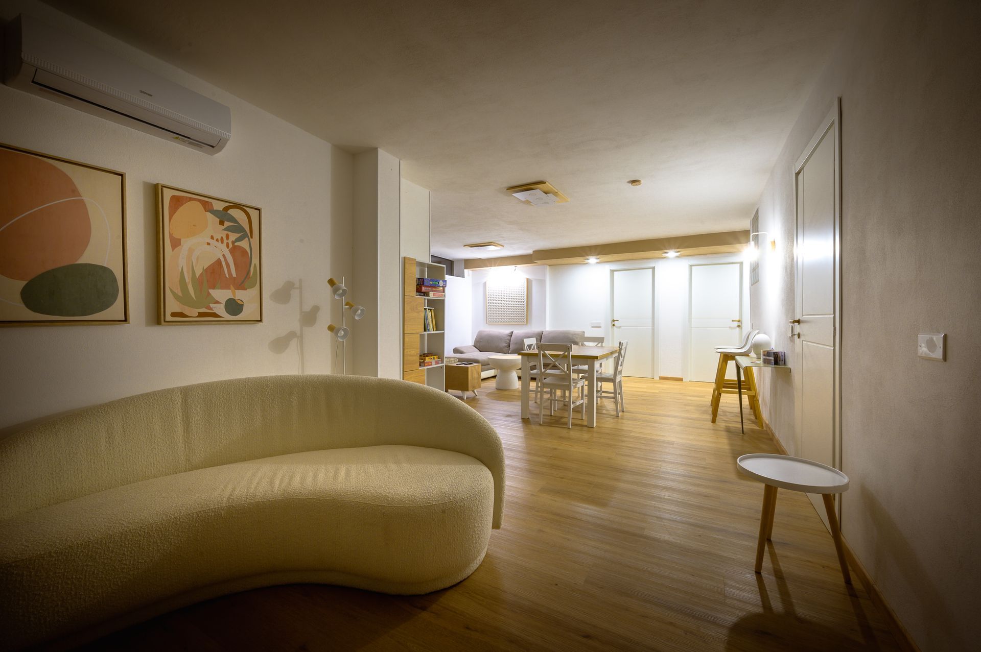 Soggiorno con divano color crema, pavimenti in legno, opere d'arte e zona pranzo.