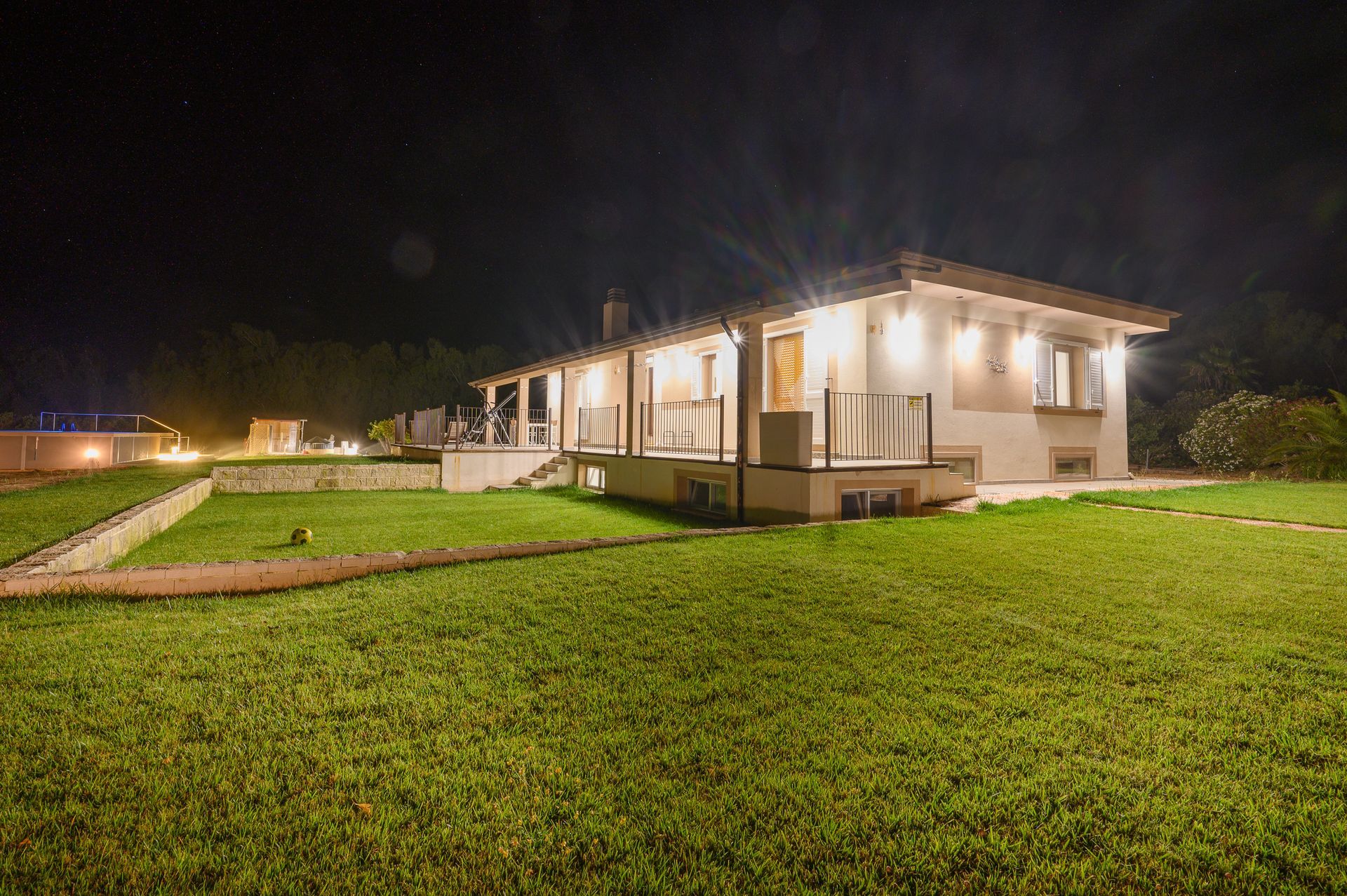 Casa illuminata di notte, con luci intense e un grande prato verde.