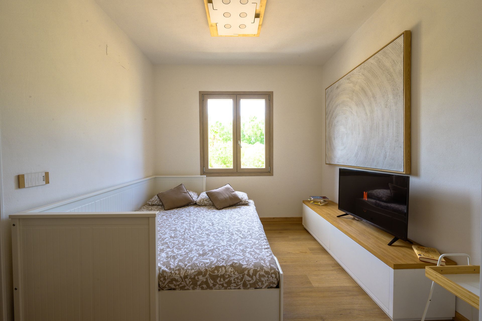 Camera da letto stretta con letto, TV, finestra e parete con opere d'arte astratte.