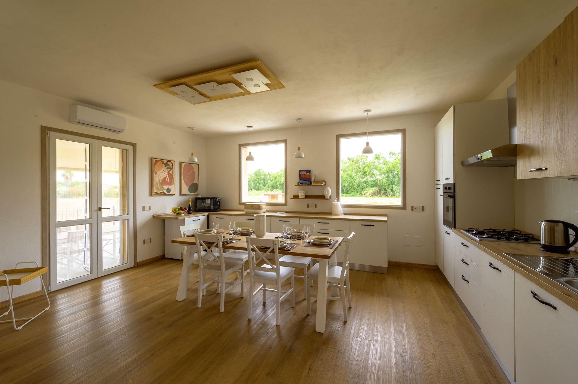 Cucina luminosa con mobili bianchi, tavolo e sedie in legno e accesso all'esterno.