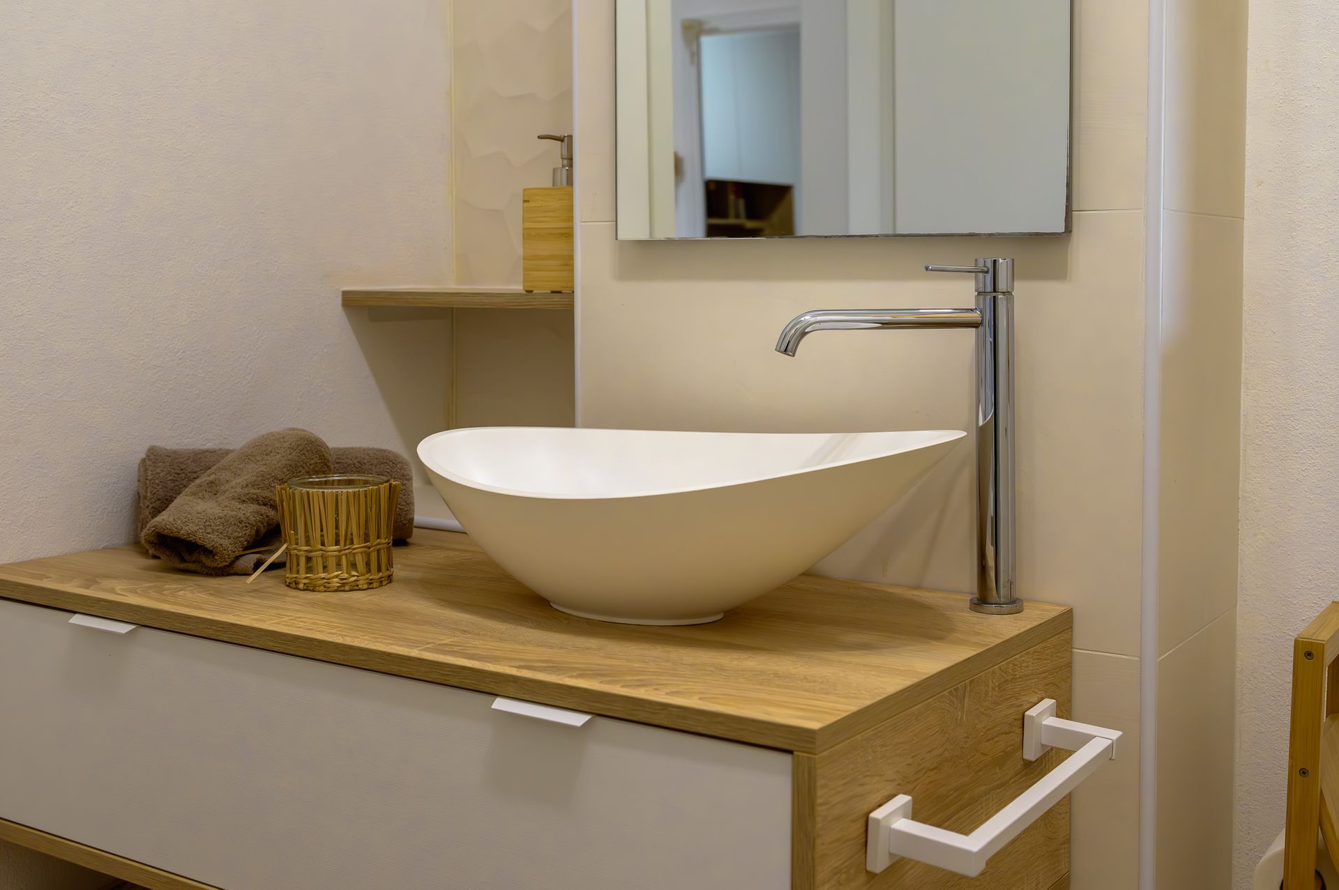 Bagno con lavabo ovale bianco su mobile in legno chiaro. Pareti beige e specchio.