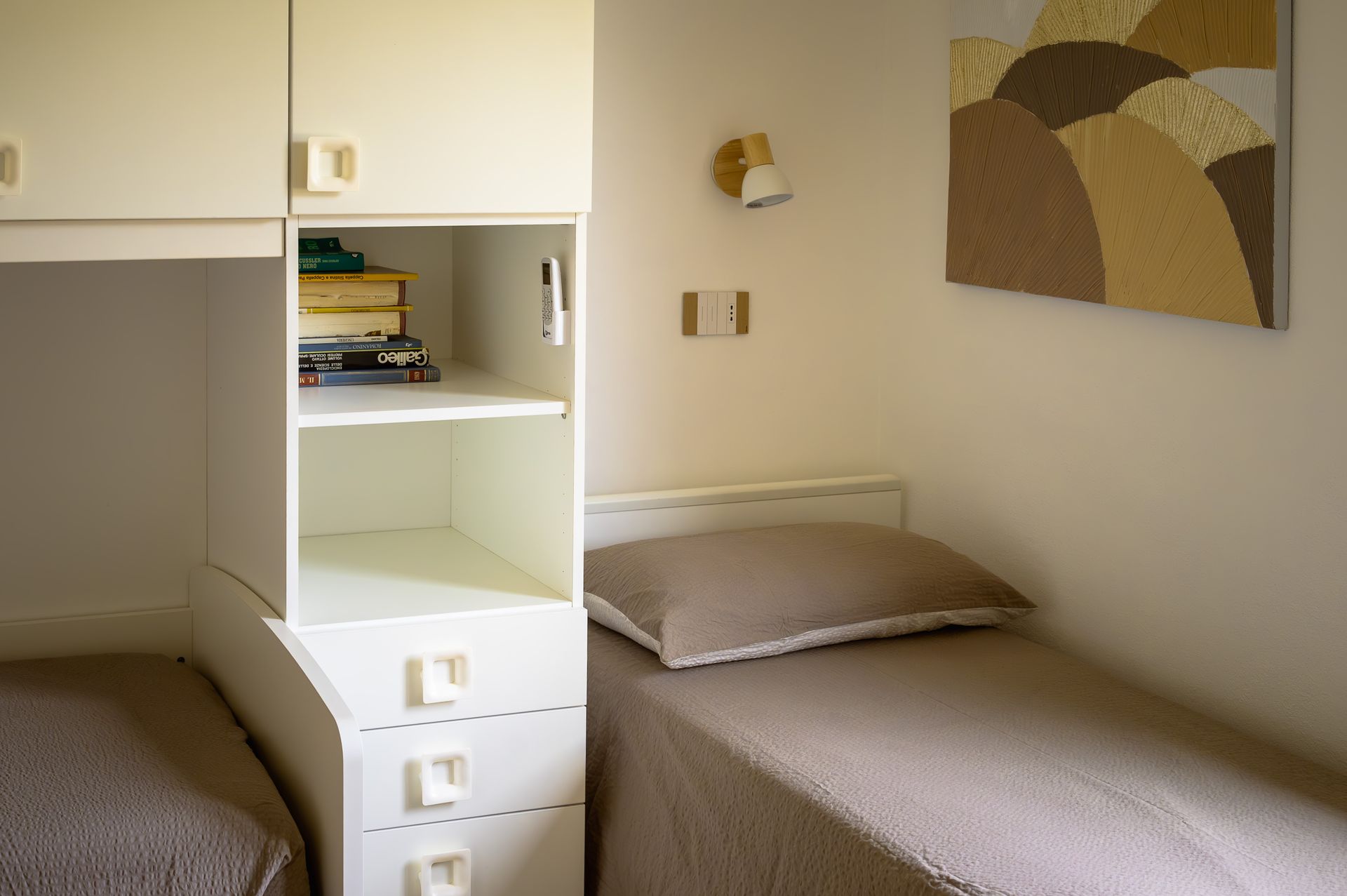 Piccola camera da letto con due letti singoli, un mobile contenitore incorporato e una lampada a parete.