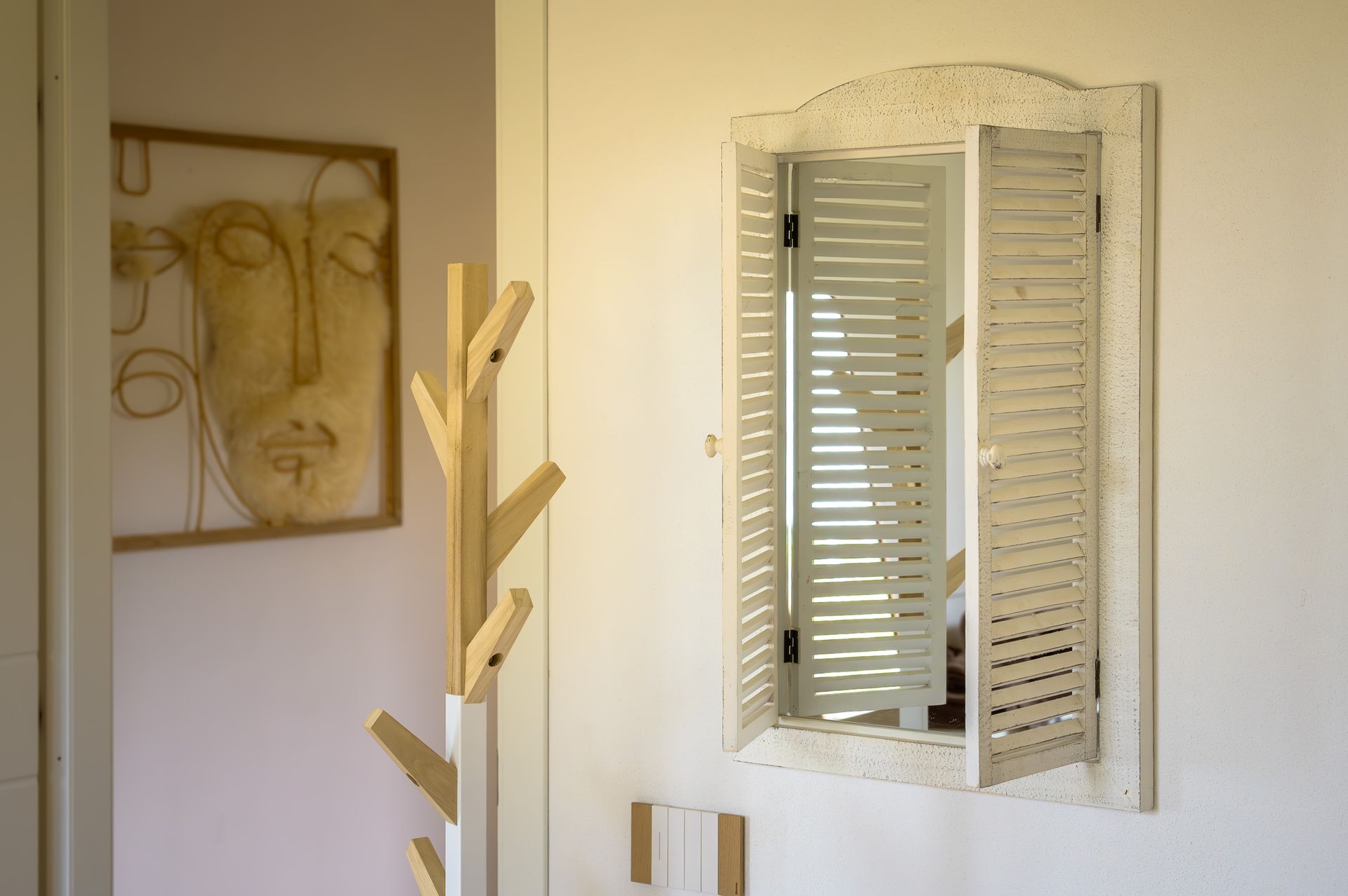 Corridoio con uno specchio bianco con persiane, quadri e un attaccapanni.