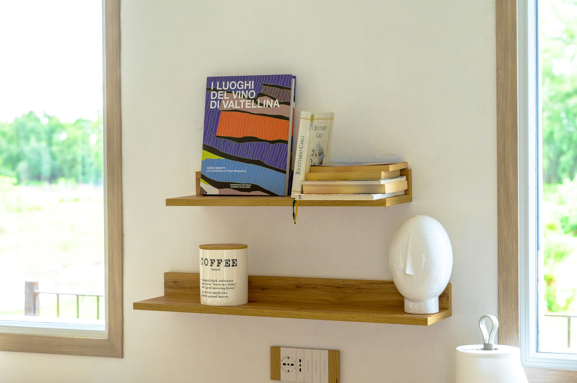 Due scaffali di legno su una parete bianca con libri, una candela e una scultura bianca a forma di uovo.