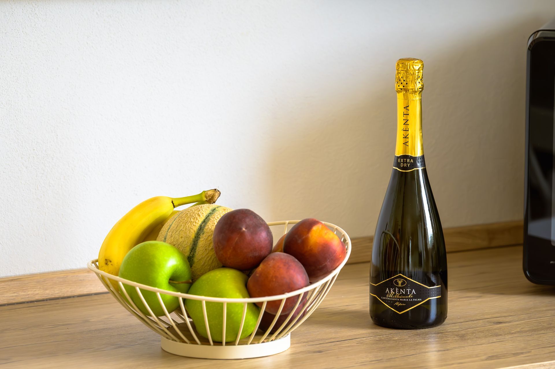 Fruttiera con mele, pesche, banane e melone accanto a una bottiglia di champagne.