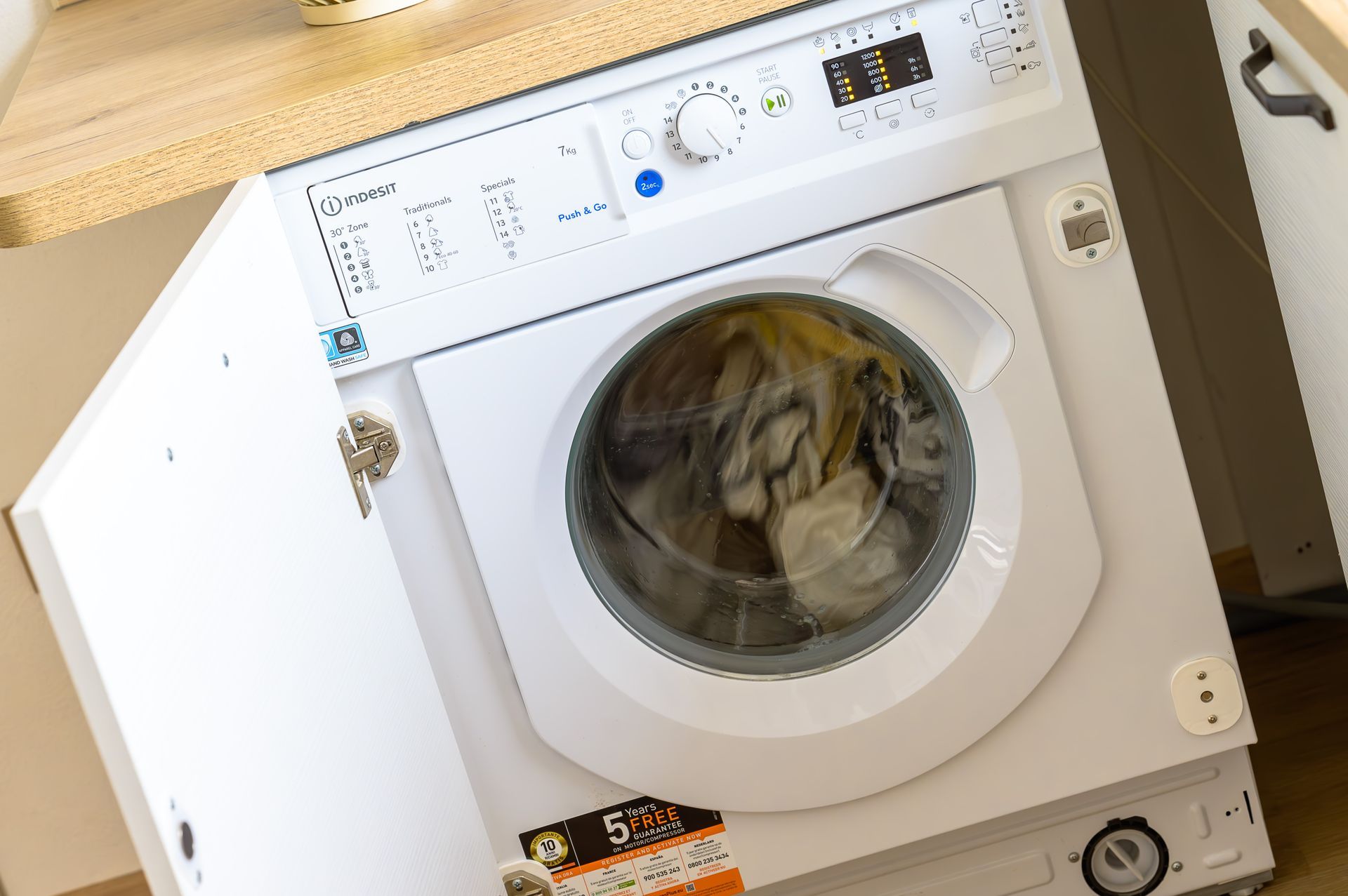 Lavatrice bianca con vestiti dentro, sotto un bancone di legno.