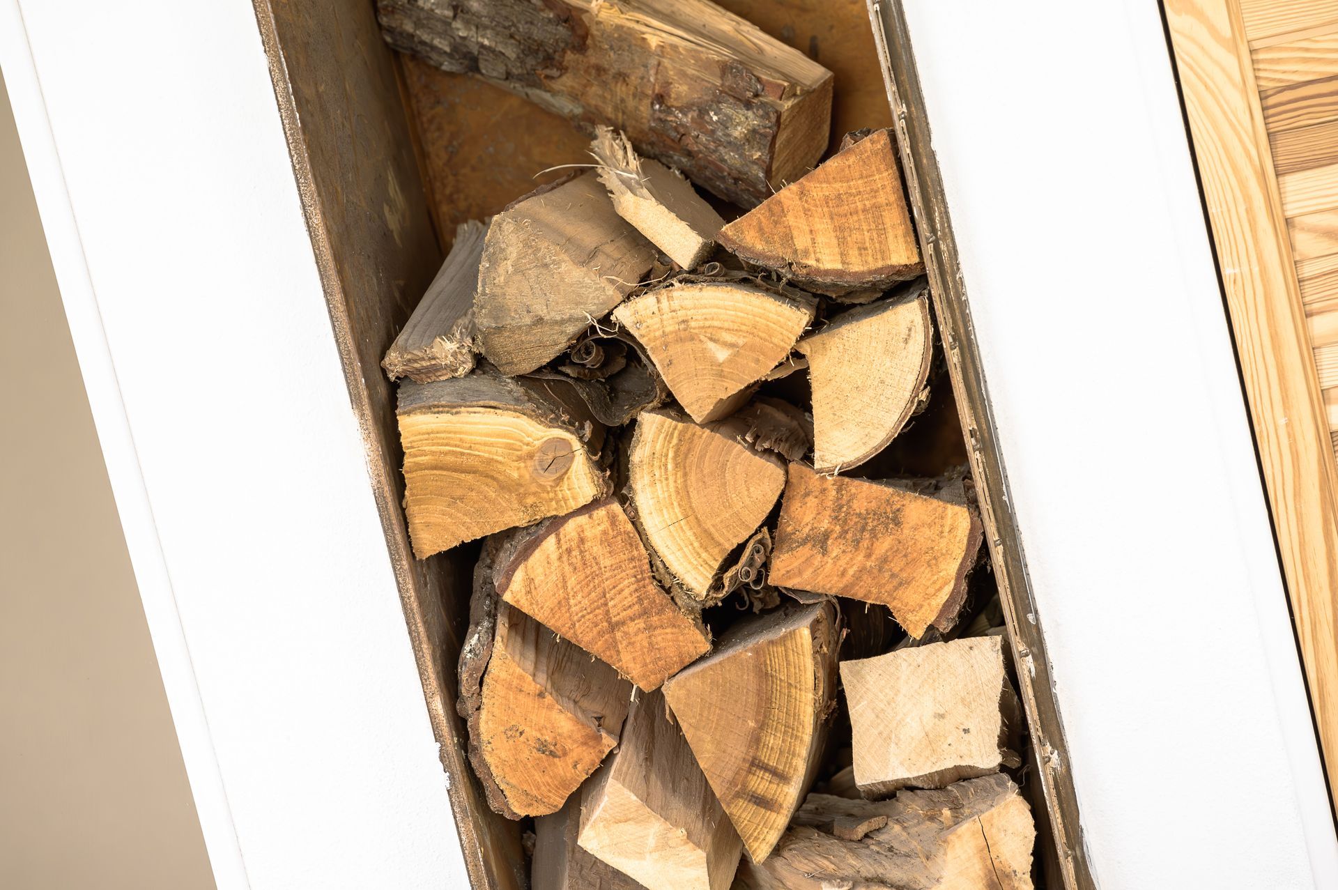 Ceppi di legna accatastati in una scatola rettangolare bianca, pronti per il camino.