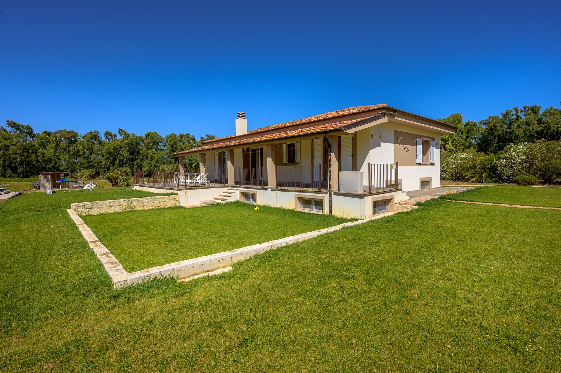 Casa con tetto di tegole marroni, pareti bianche e prato verde sotto un cielo azzurro.
