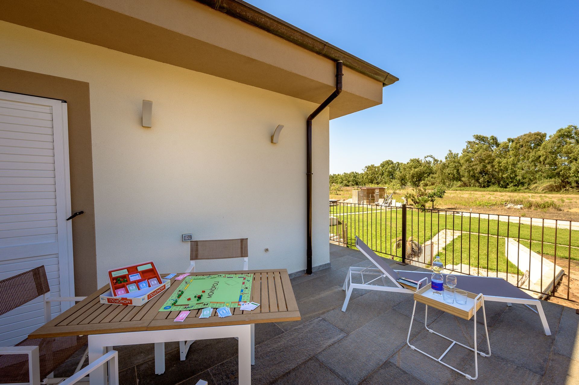 Patio con tavolo, sedie, gioco da tavolo e sedia a sdraio con vista sul paesaggio verdeggiante sotto il cielo azzurro.