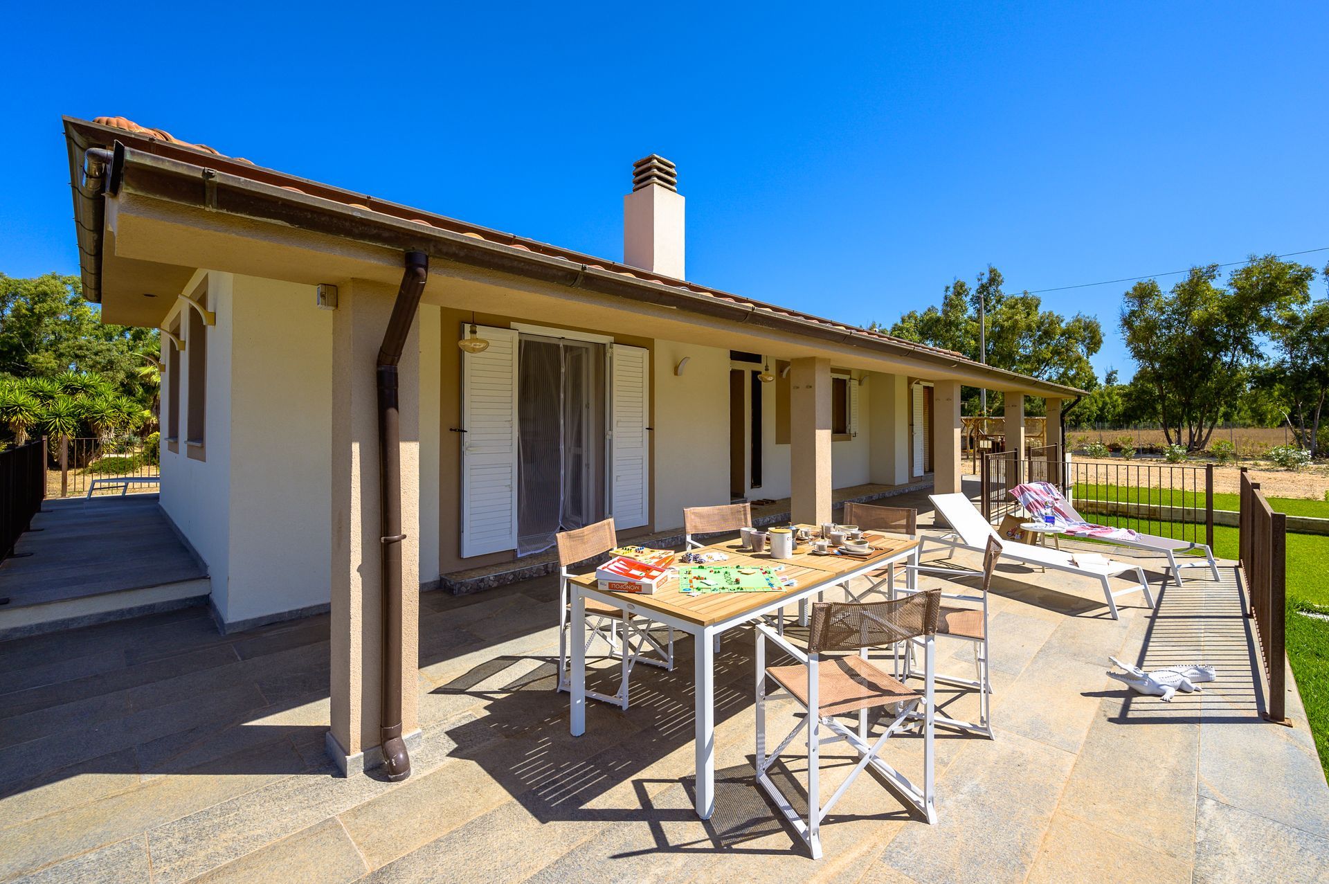 Casa beige con zona pranzo all'aperto, prato e cielo azzurro terso.