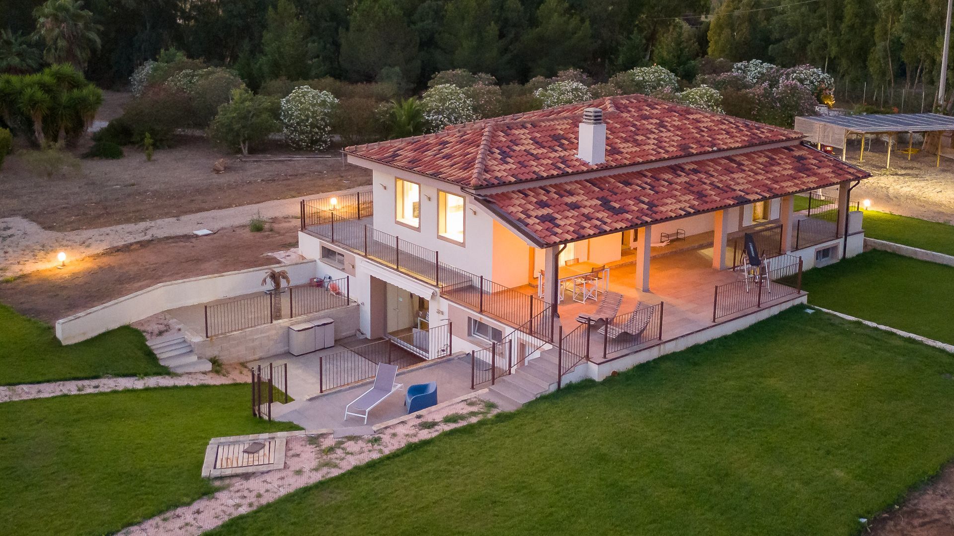 Casa beige a due piani con tetto in tegole arancioni e ampio patio coperto in un campo erboso.