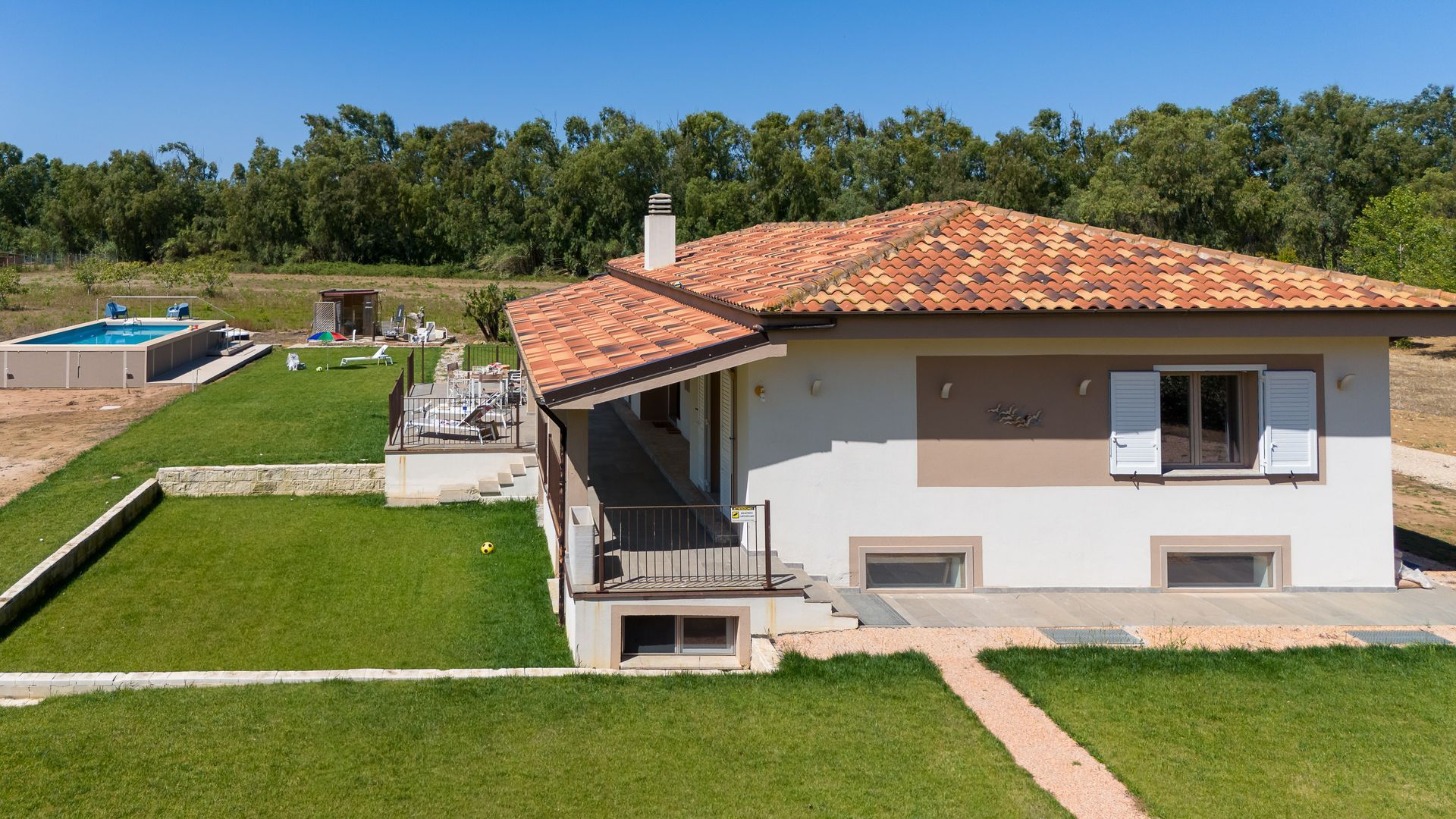 Casa con tetto in tegole arancioni, prato verde e piscina in posizione soleggiata.