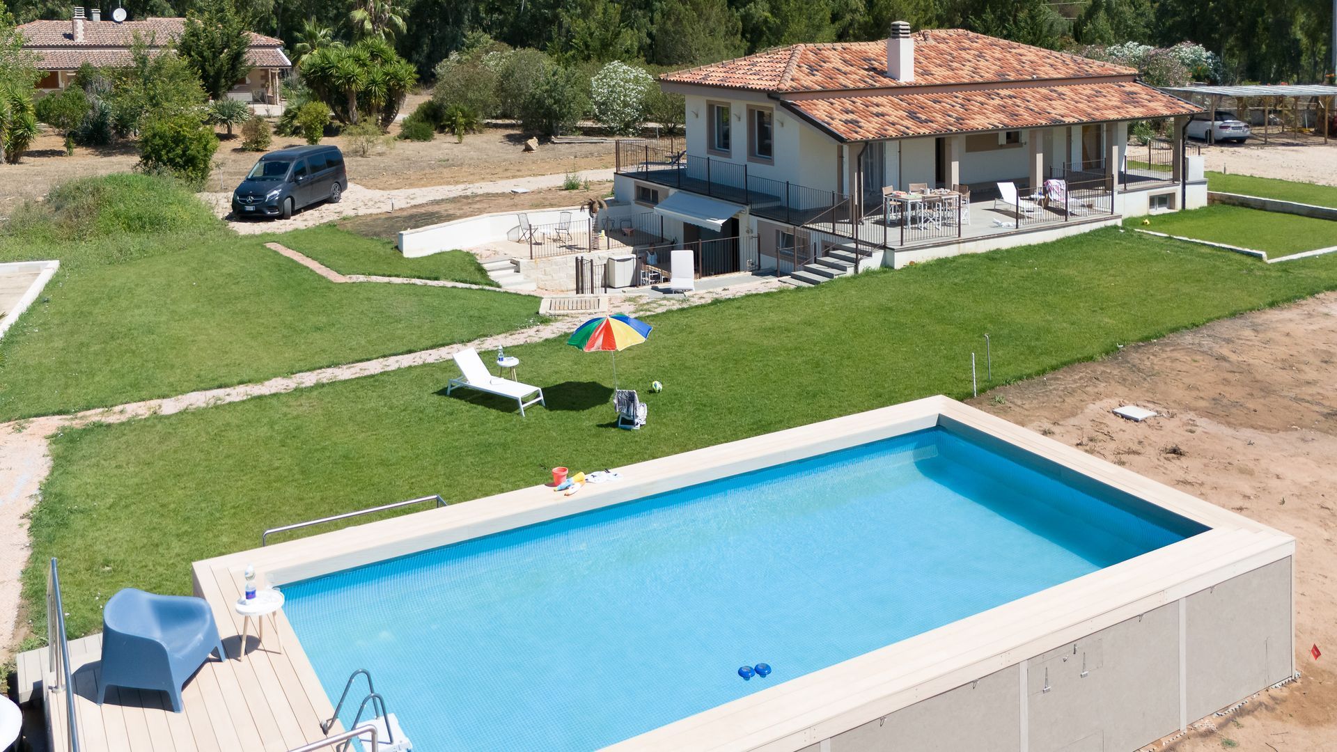 Casa con piscina, prato verde e auto; giornata soleggiata.
