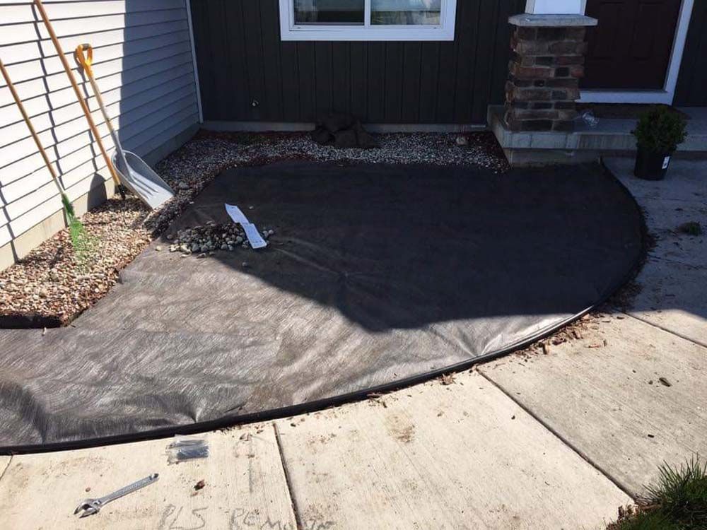 A Concrete Patio With a Black Tarp on It in Front of a House