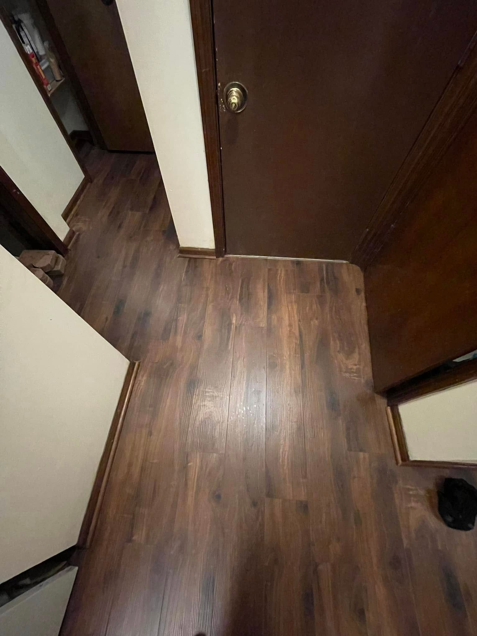 Dark wood-look flooring in a room with a closed brown door and white trim.