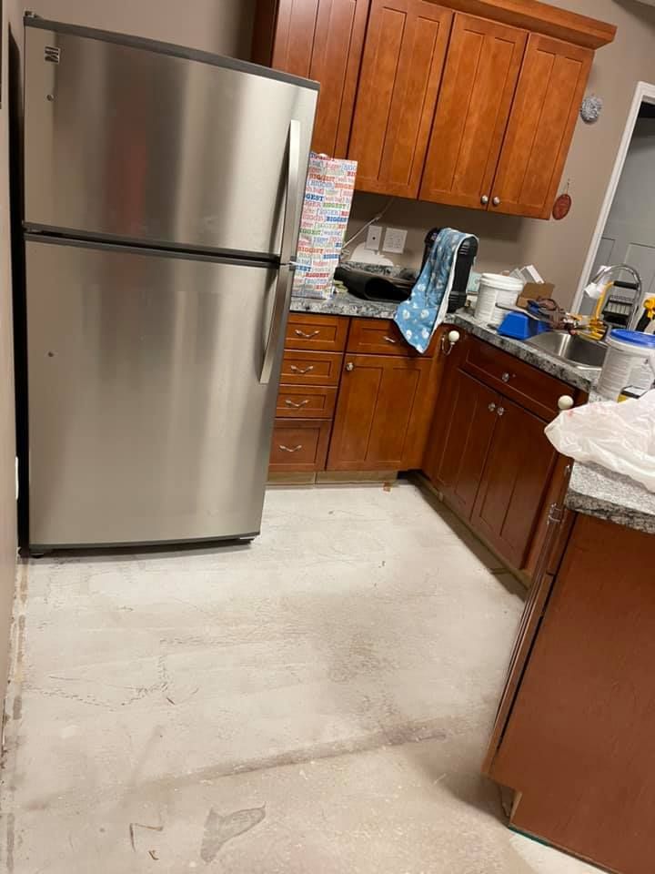 Kitchen with stainless steel refrigerator, wooden cabinets, and gray countertops, possibly under renovation.