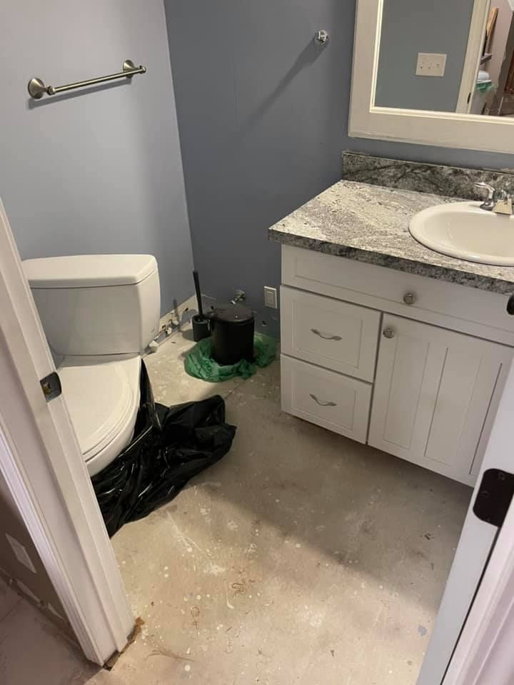 Bathroom with white toilet, vanity, and gray countertop. Unfinished concrete floor, blue walls, black trash bag.