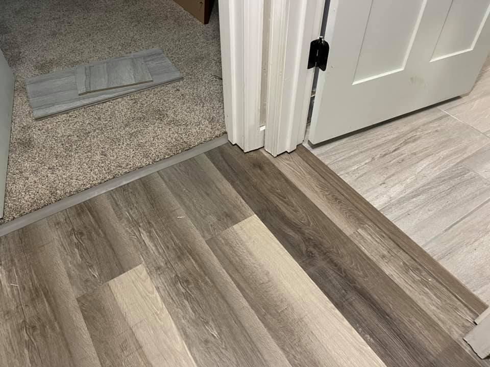 Transition between flooring types: wood-look planks, carpet, and tiled surface, meeting at a doorway.