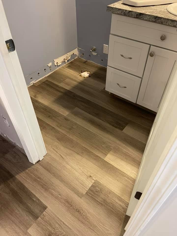 Bathroom with wood-look flooring. Light blue walls, white vanity, and open doorway on either side.